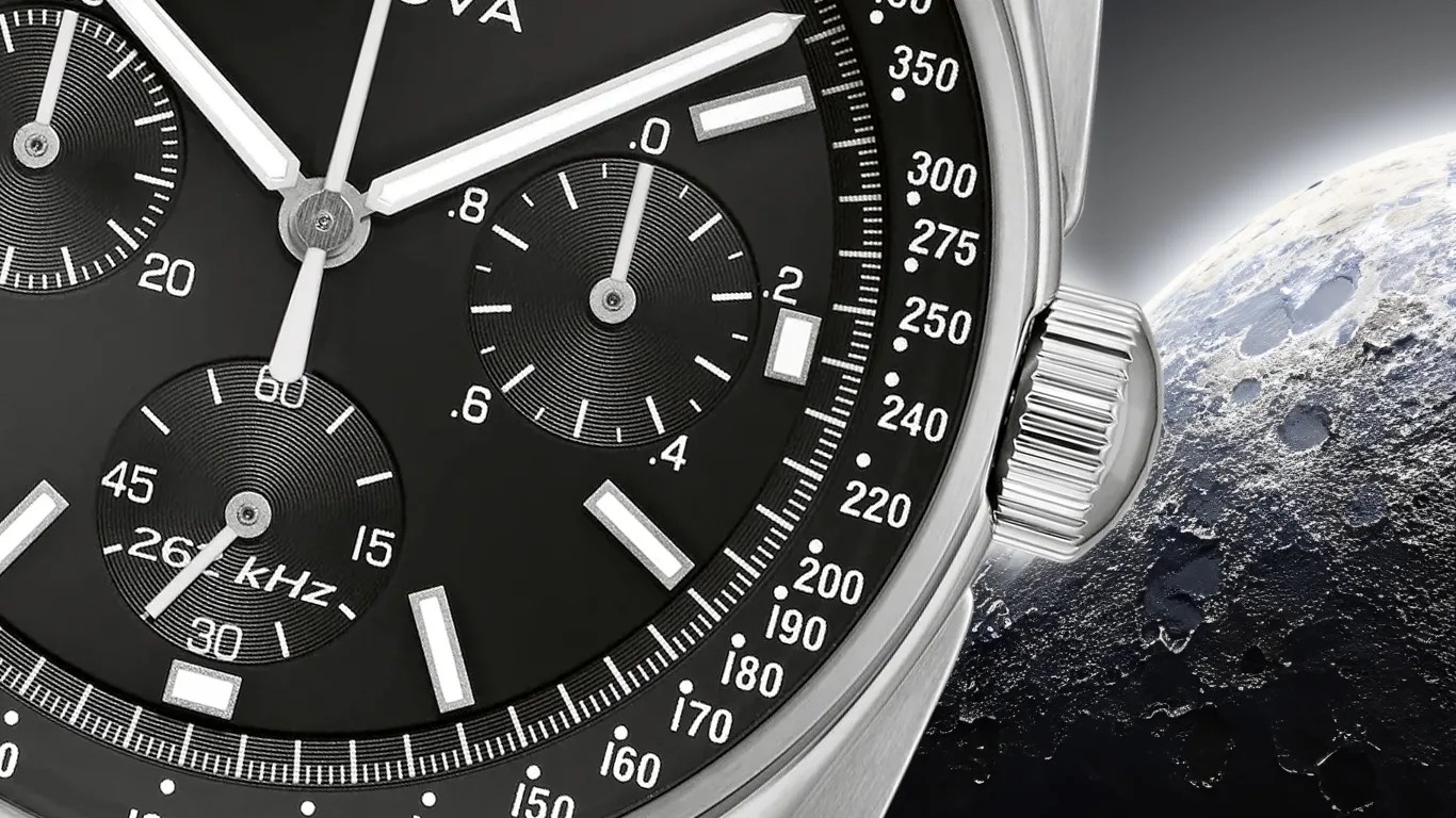 Close-up of a black chronograph watch face with white markers and a silver crown, next to a textured moon surface.