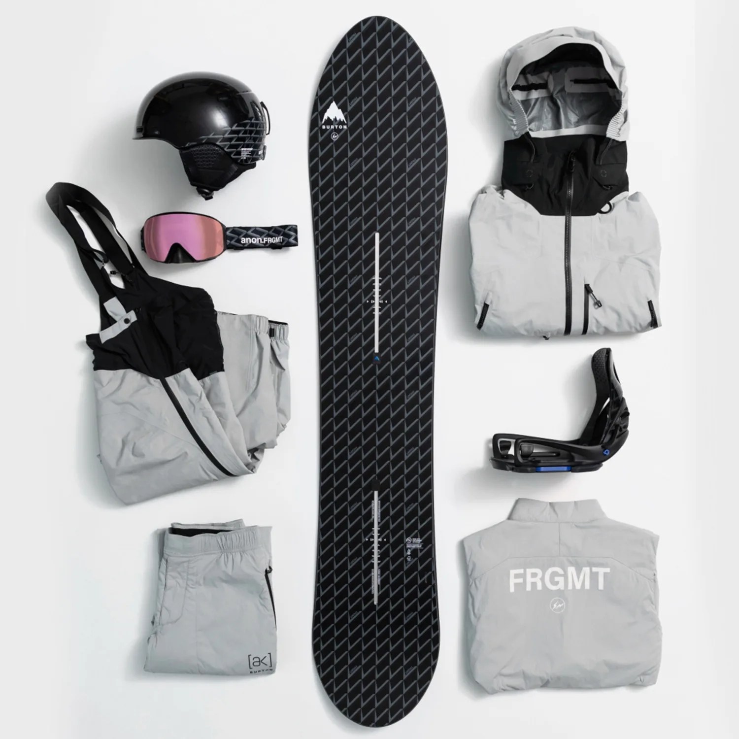 Black and gray Burton snowboard with gray snowboarding jacket, bib pants, pants, black helmet, goggles, and black bindings arranged on a white background.