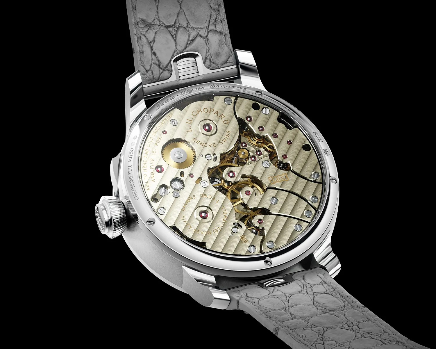 Close-up of a luxury watch's transparent case back showing intricate gold and silver mechanical movement with ruby jewels and a gray textured leather strap.
