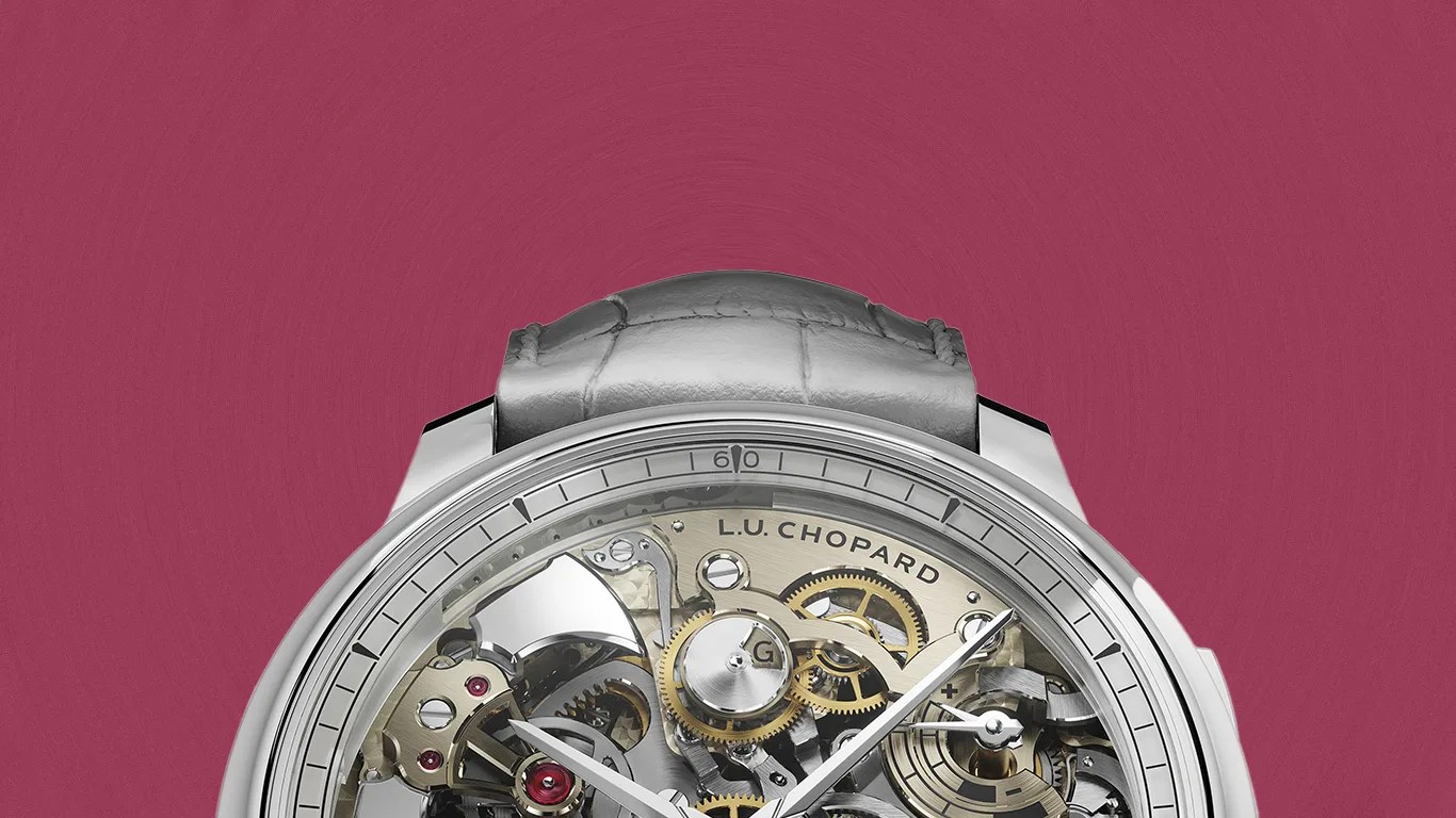 Silver Chopard L.U.C. mechanical watch with visible gears and a gray leather strap on a maroon background.