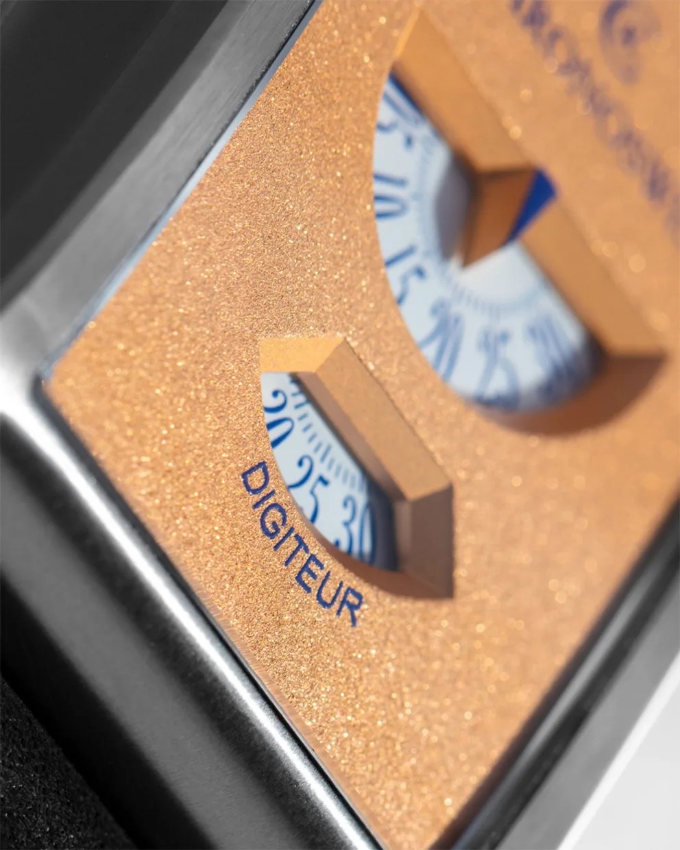 Close-up of a gold textured dial with blue numbers and the word "DIGITEUR" on a metallic device.