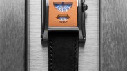 Rectangular watch with orange dial featuring two small windows displaying blue numbers and a black leather strap.