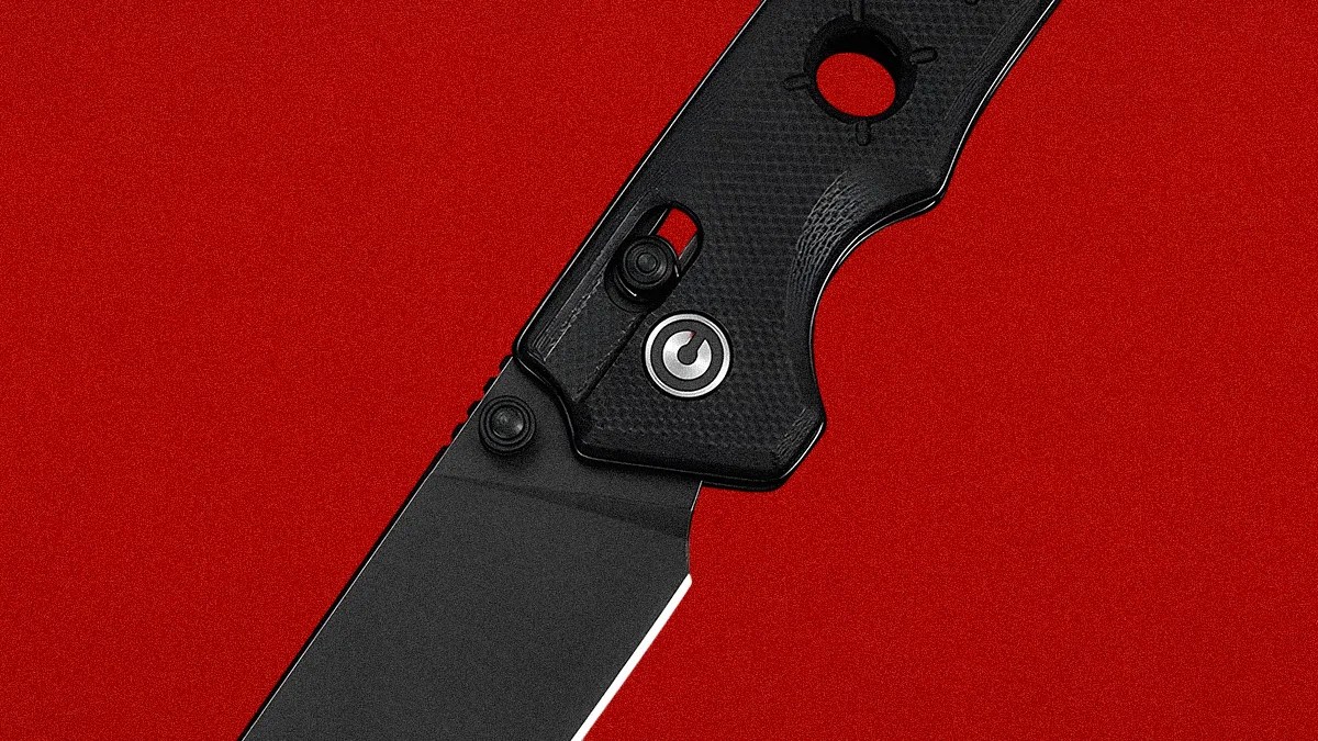Black folding knife with textured handle and circular hole near the pivot on a red background.