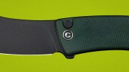 Close-up of a folding knife with a black blade and textured dark green handle on a lime green background.