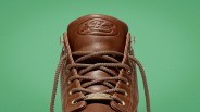 Brown leather sneaker tongue with "le Fleur" embossed logo and matching brown laces against a green background.