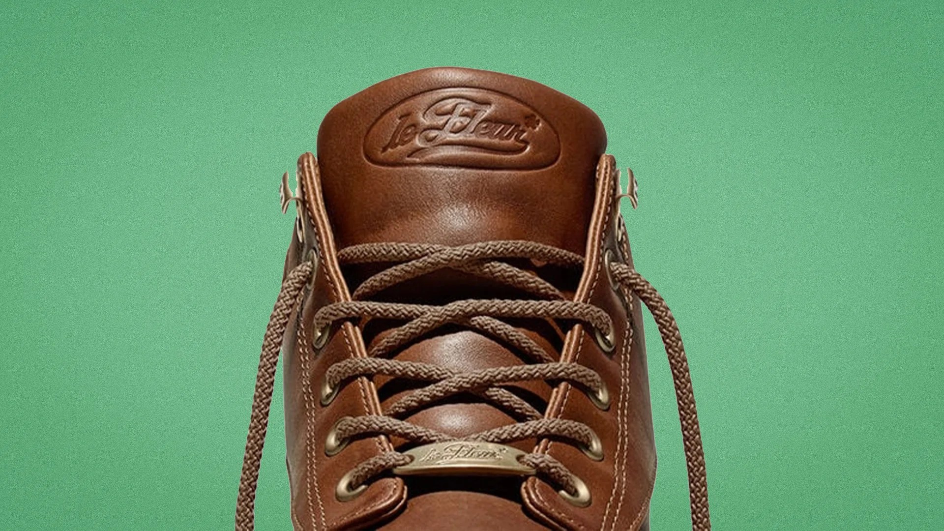 Brown leather sneaker tongue with "le Fleur" embossed logo and matching brown laces against a green background.