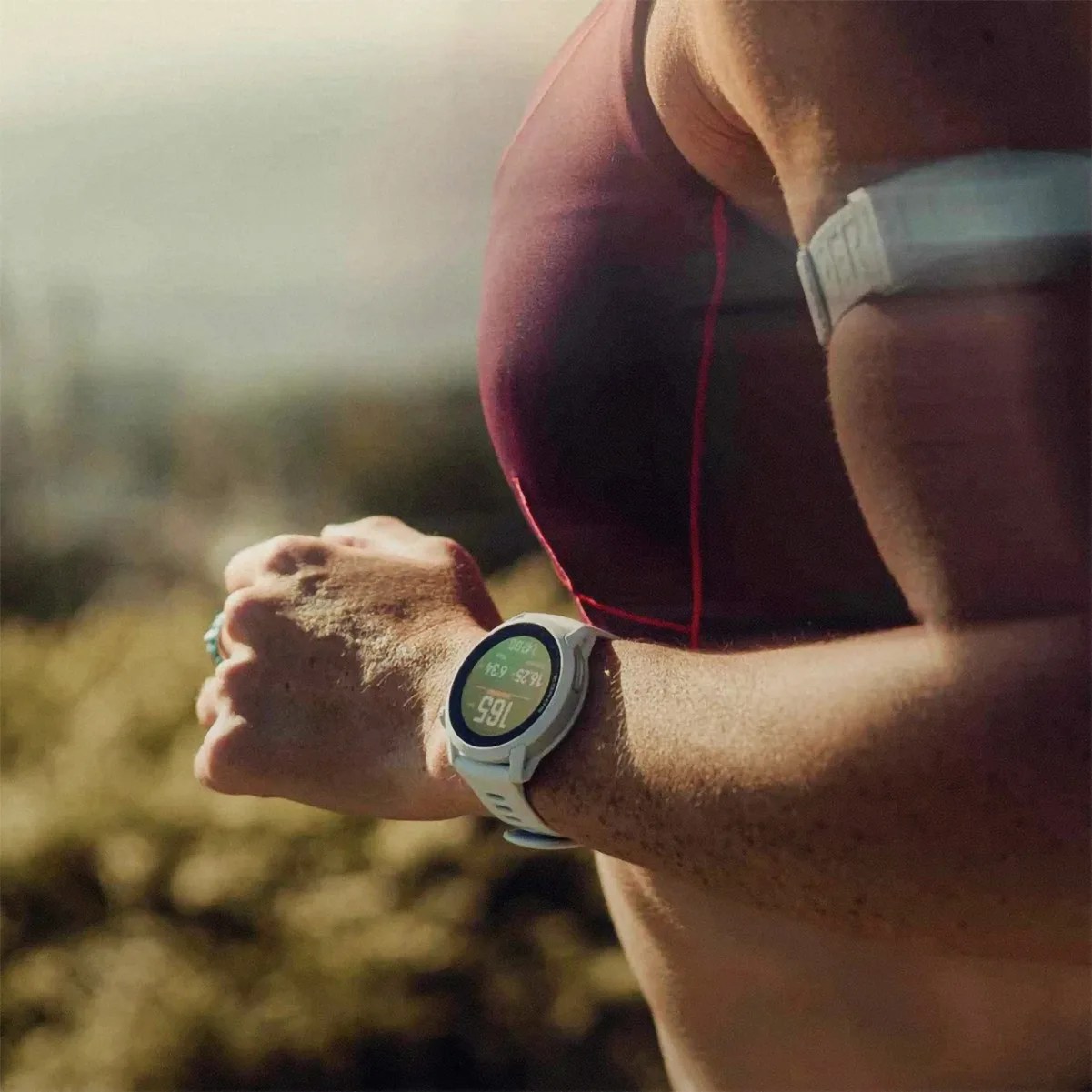 Close-up of a person wearing a white fitness watch and a maroon sports top while running outdoors.