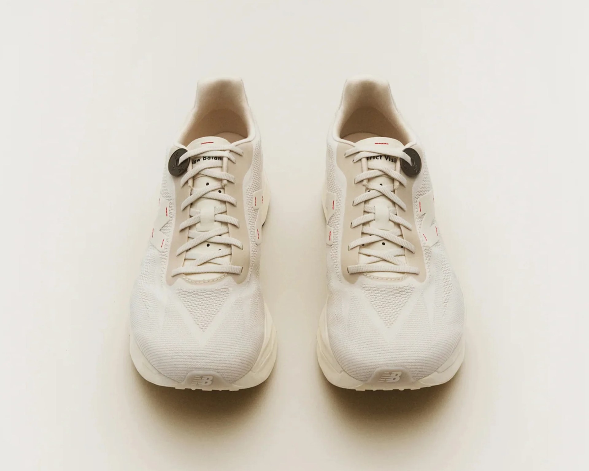 Pair of off-white New Balance running shoes with mesh uppers and beige accents, viewed from above.