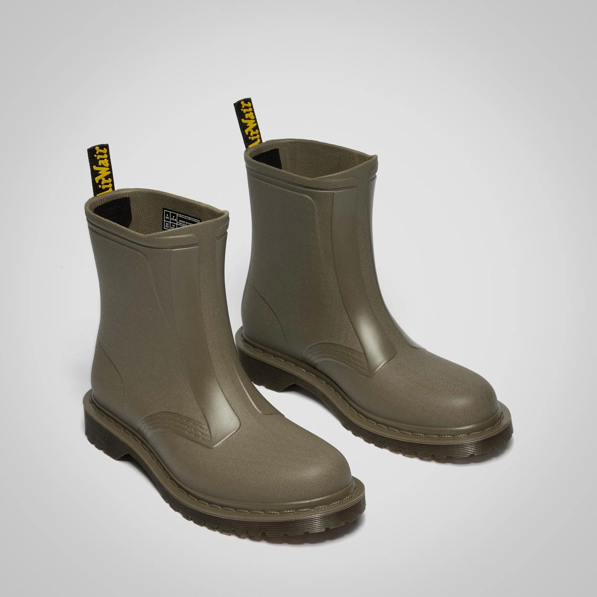 Pair of olive green matte rubber ankle boots with black and yellow pull tabs and thick soles on a gray background.
