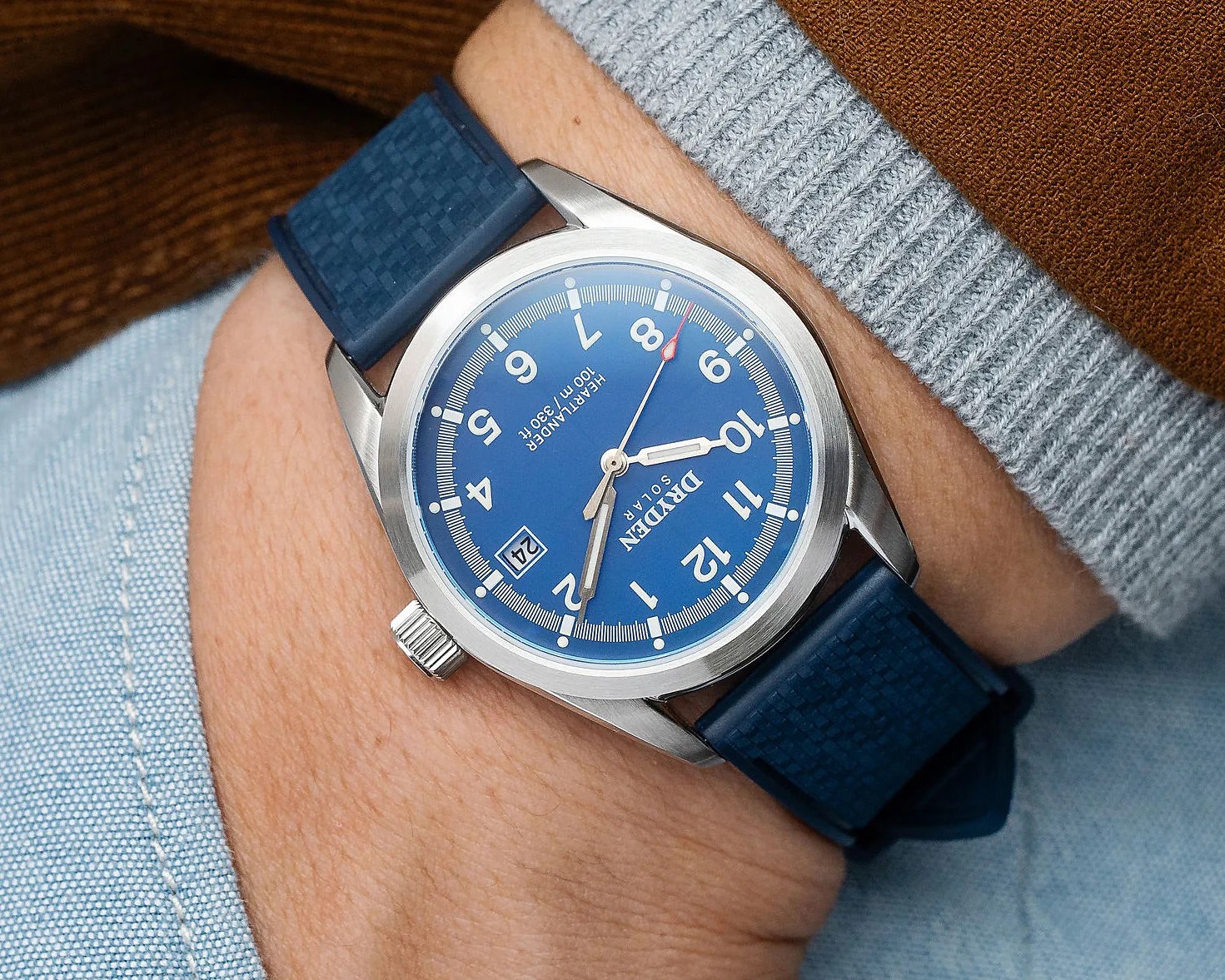 Wristwatch with a blue dial, white numerals, date window, and blue textured strap worn on a wrist.