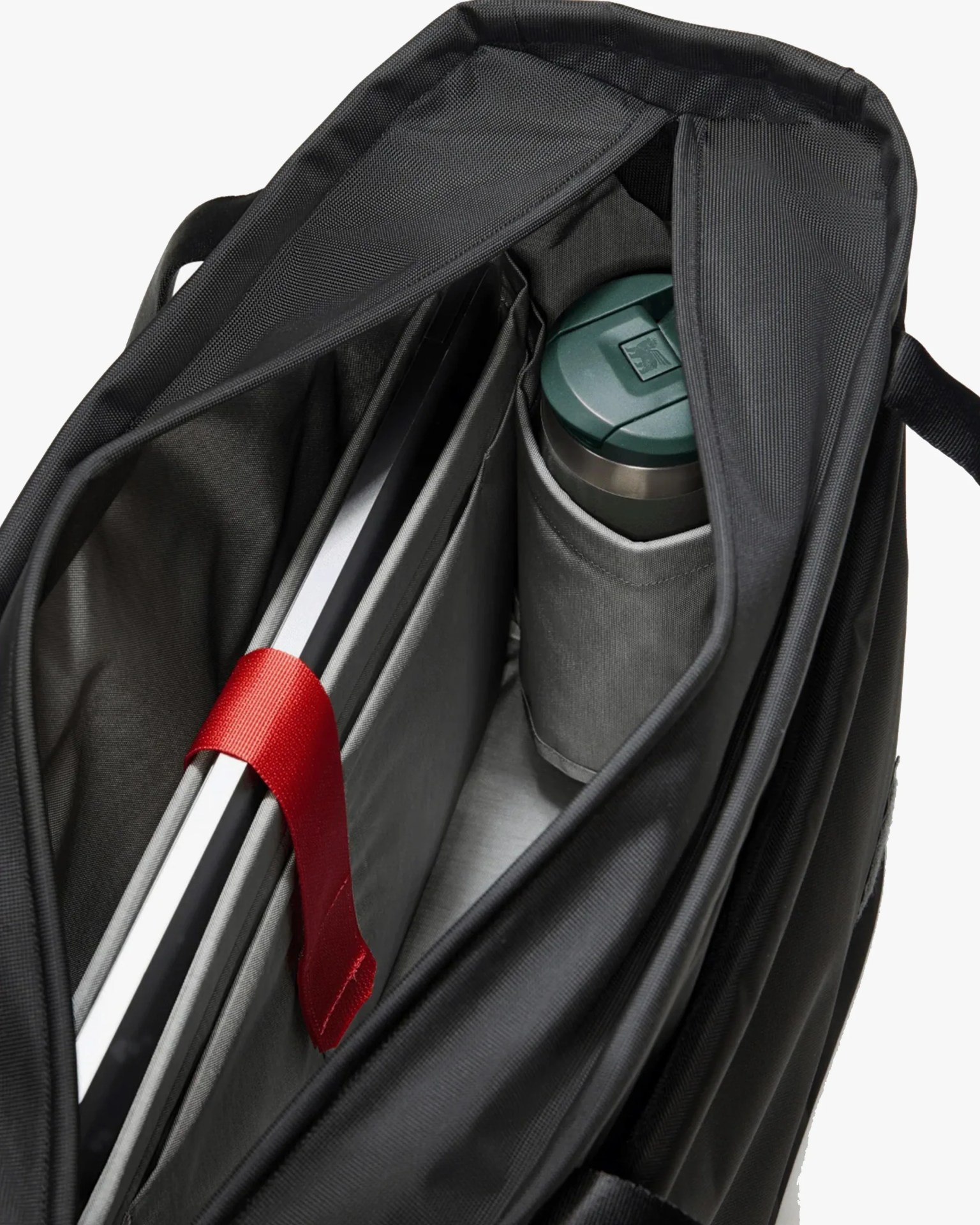 Black laptop bag interior showing a laptop secured with a red strap and a green-lidded thermos in a side pocket.