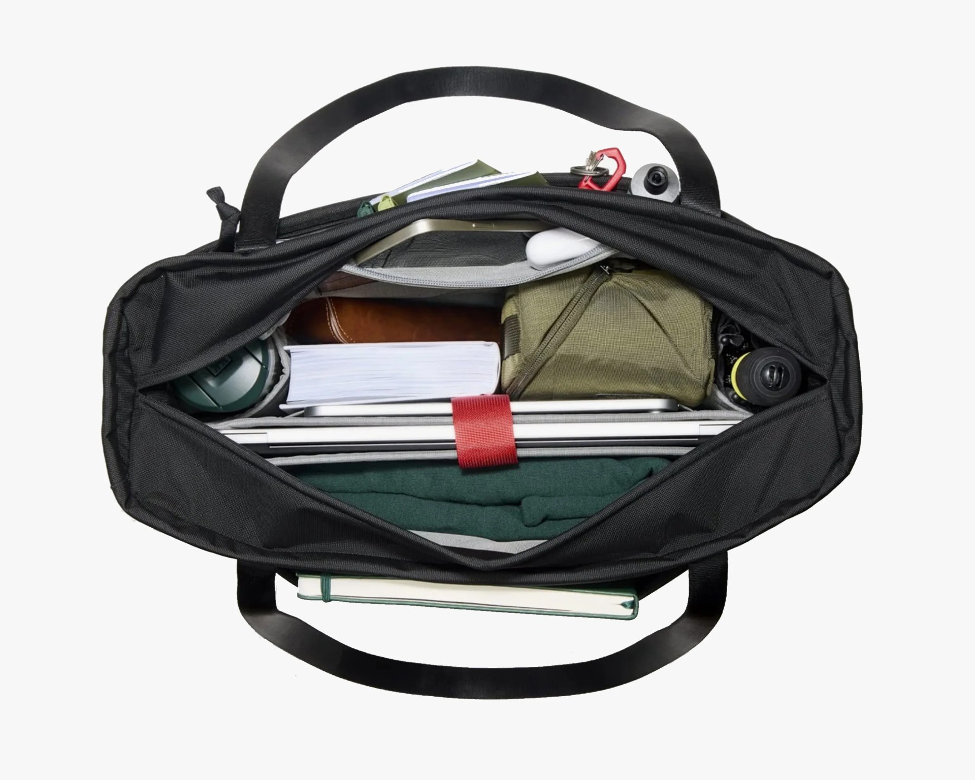 Top view of a black tote bag filled with a laptop, book, green pouch, water bottle, and other personal items.