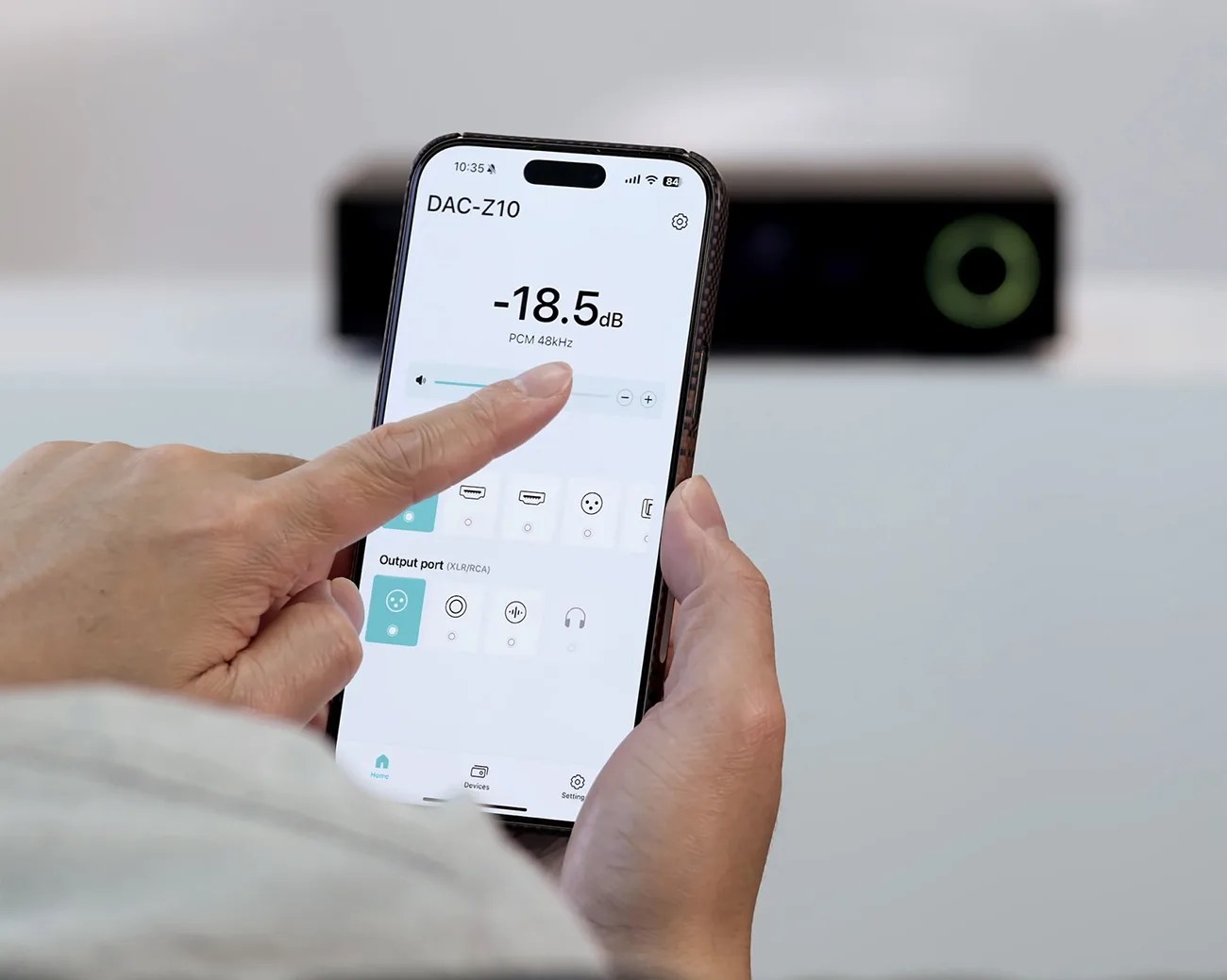 Hand holding a smartphone showing a DAC-Z10 audio control app with volume set to -18.5 dB.