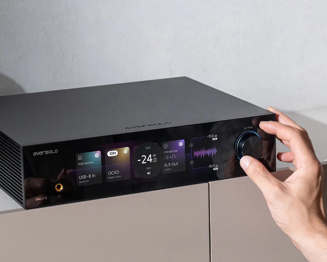 Black EverSolo DAC-Z10 digital-to-analog converter with touchscreen display and a hand adjusting the volume knob.