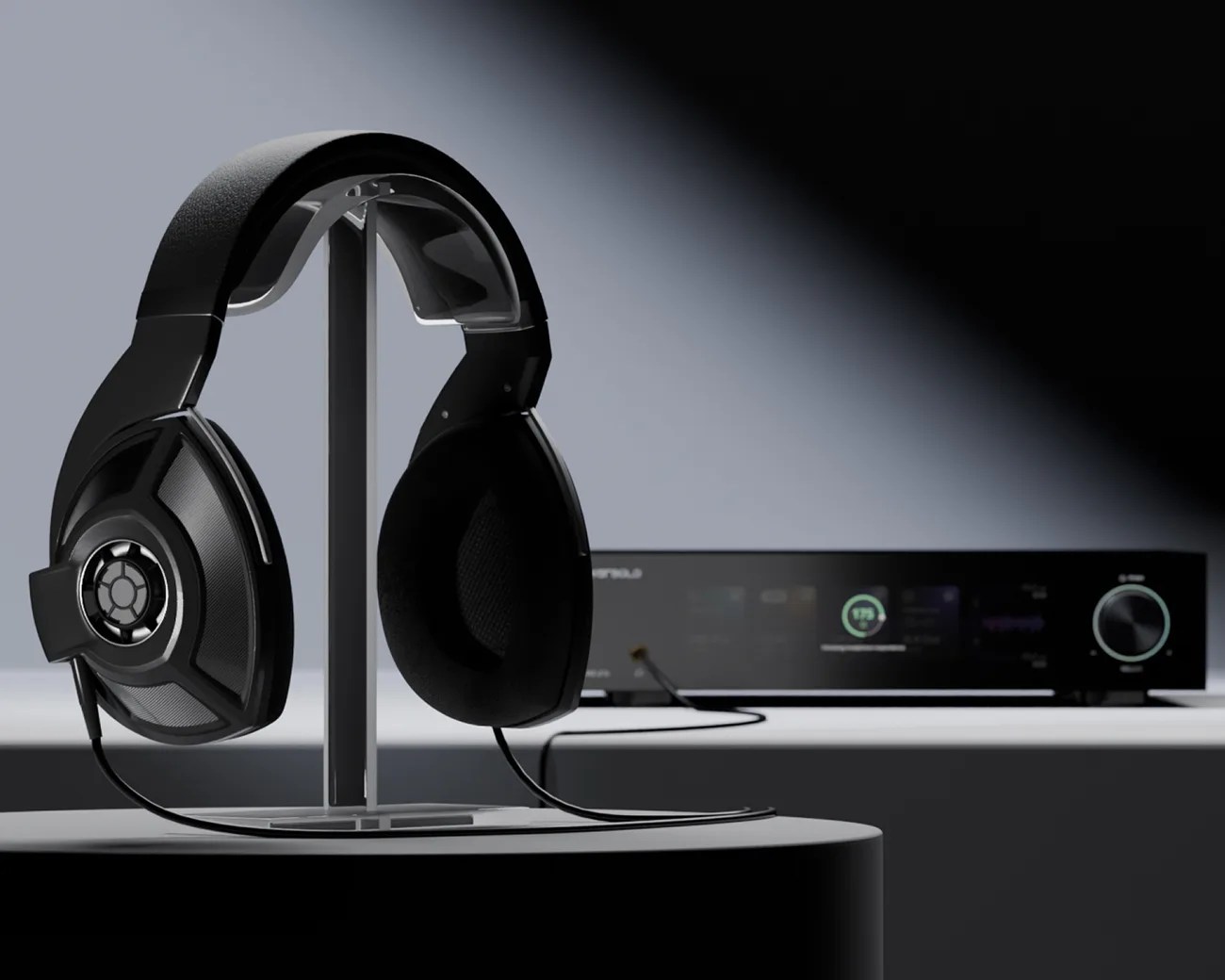 Black over-ear headphones with mesh ear cups on a metal stand, connected to a black audio device in the background.