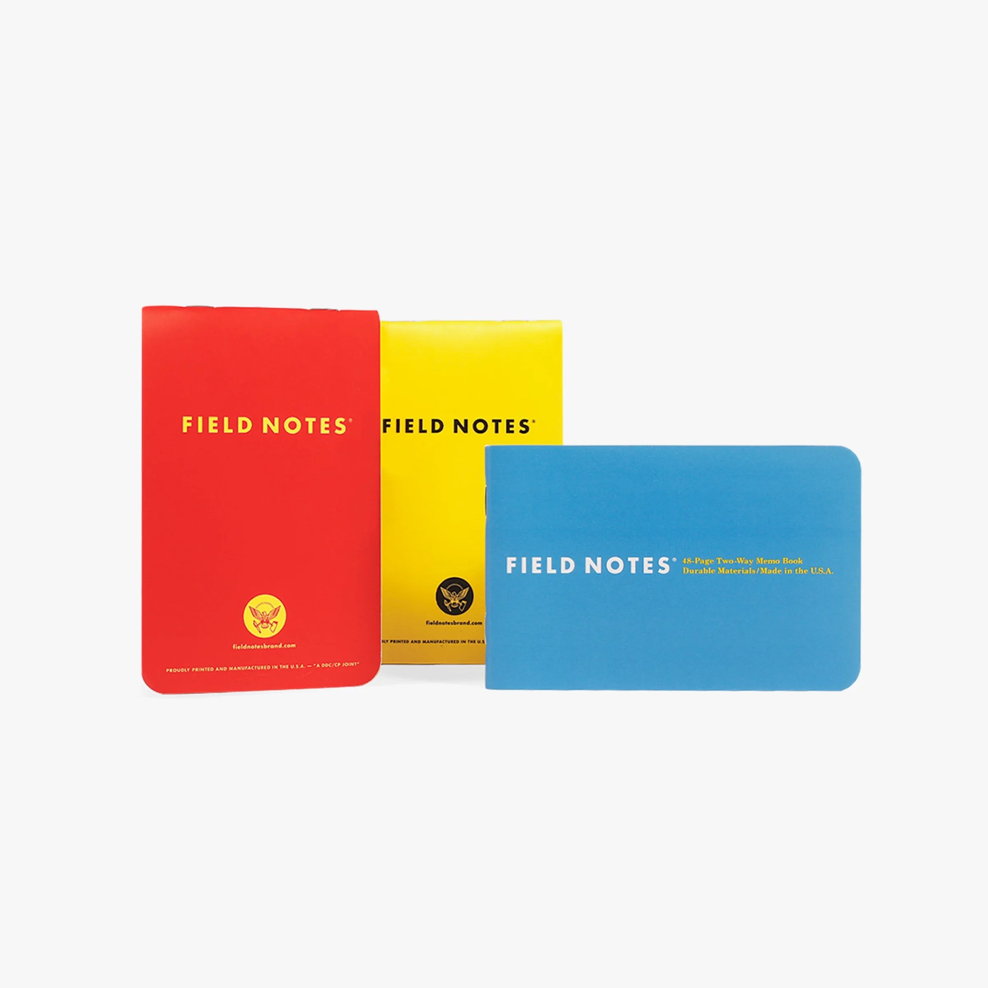 Three Field Notes memo books in red, yellow, and blue with rounded corners and printed text on the covers.