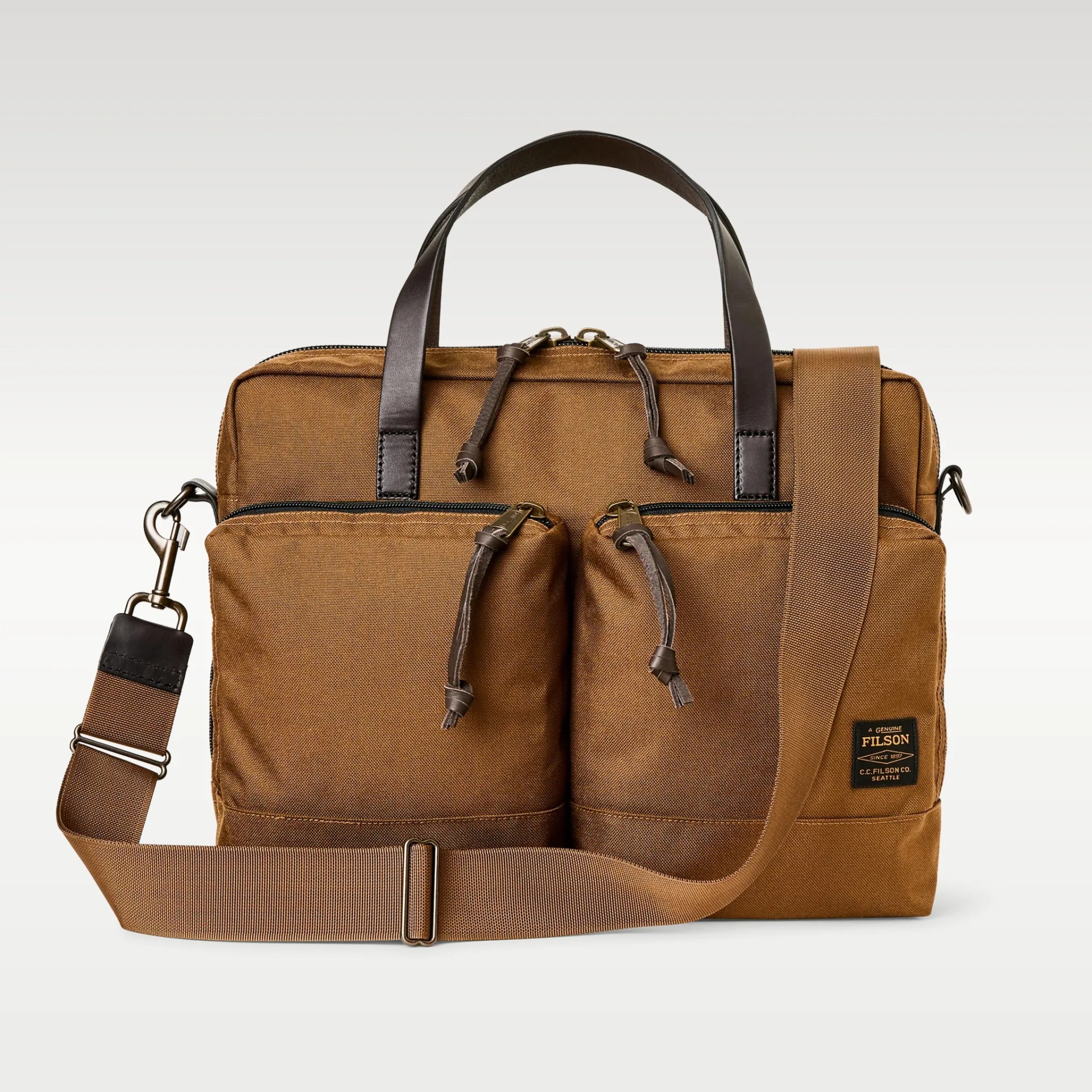 Brown Filson canvas briefcase with two front zippered pockets, dark leather handles, and an adjustable shoulder strap.