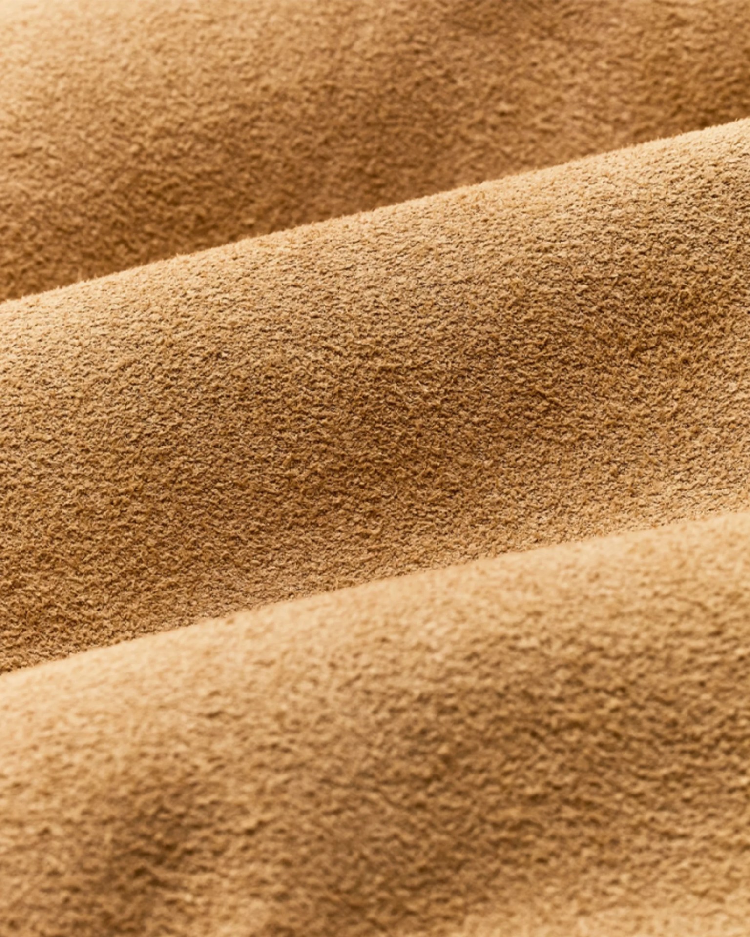 Close-up of tan suede fabric showing its soft, textured surface and fine nap.