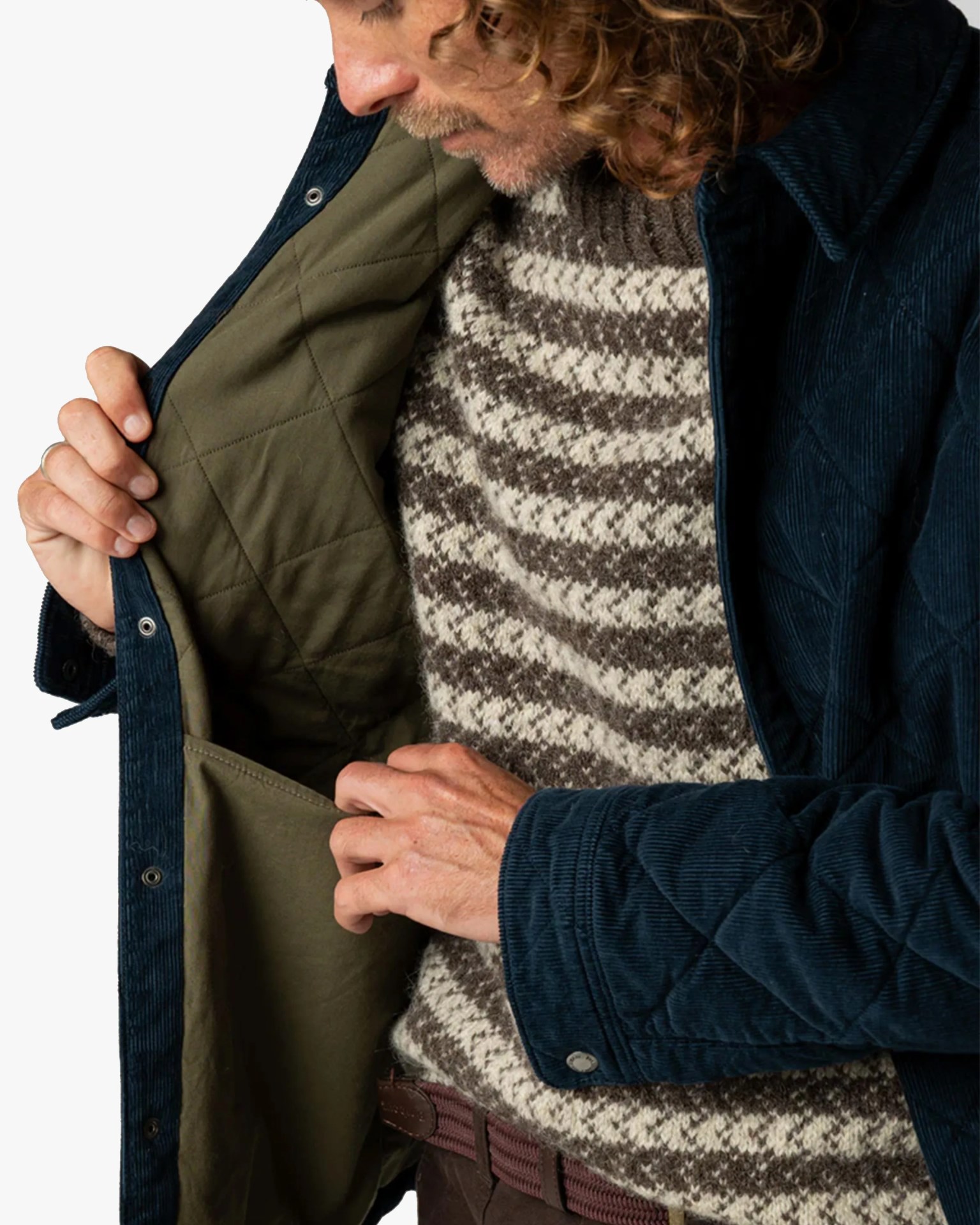 Man wearing a brown and cream patterned sweater and navy quilted corduroy jacket with olive green inner lining.