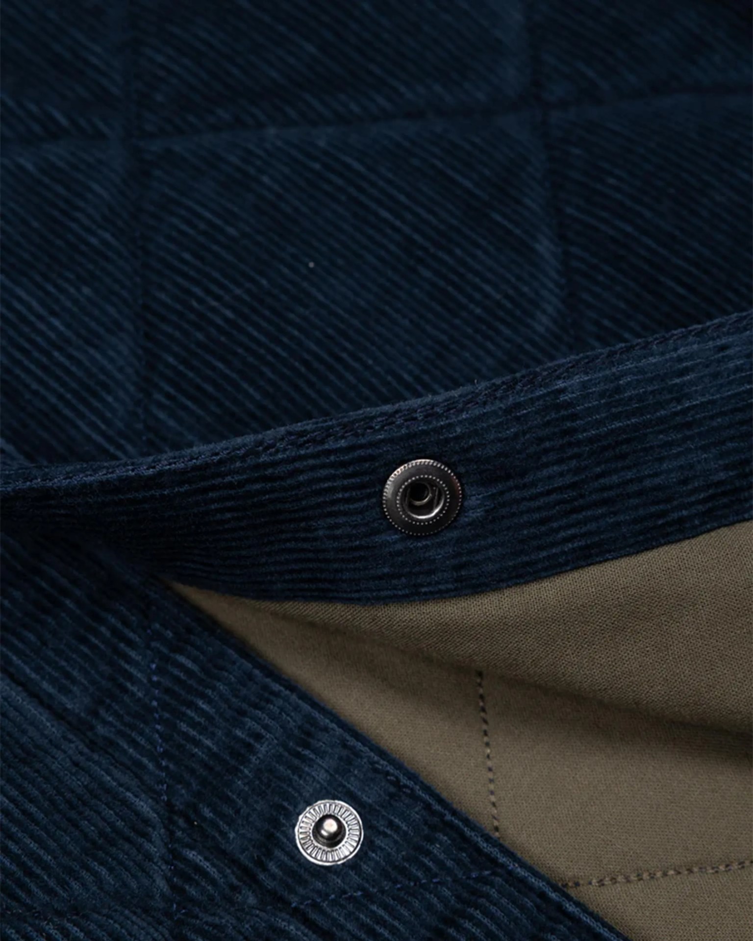 Close-up of navy blue quilted corduroy fabric with metal snap buttons and olive green lining.