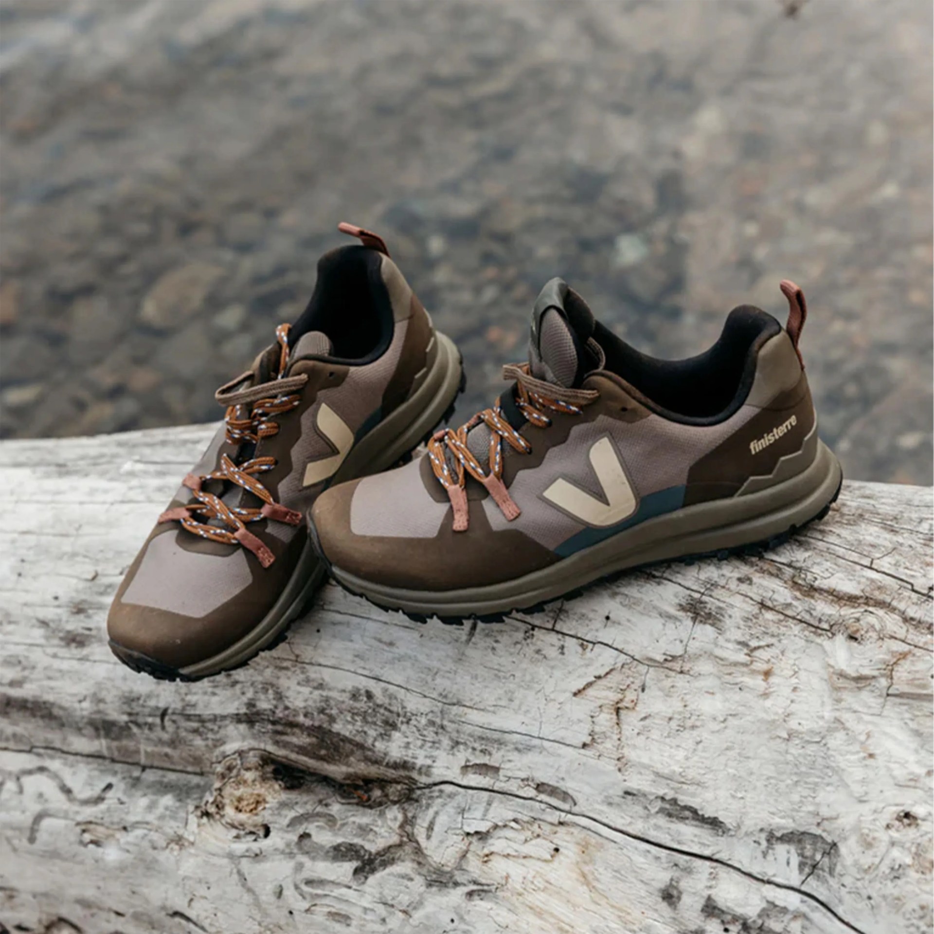 Pair of brown and beige Veja Finisterre sneakers with orange laces resting on a weathered log.