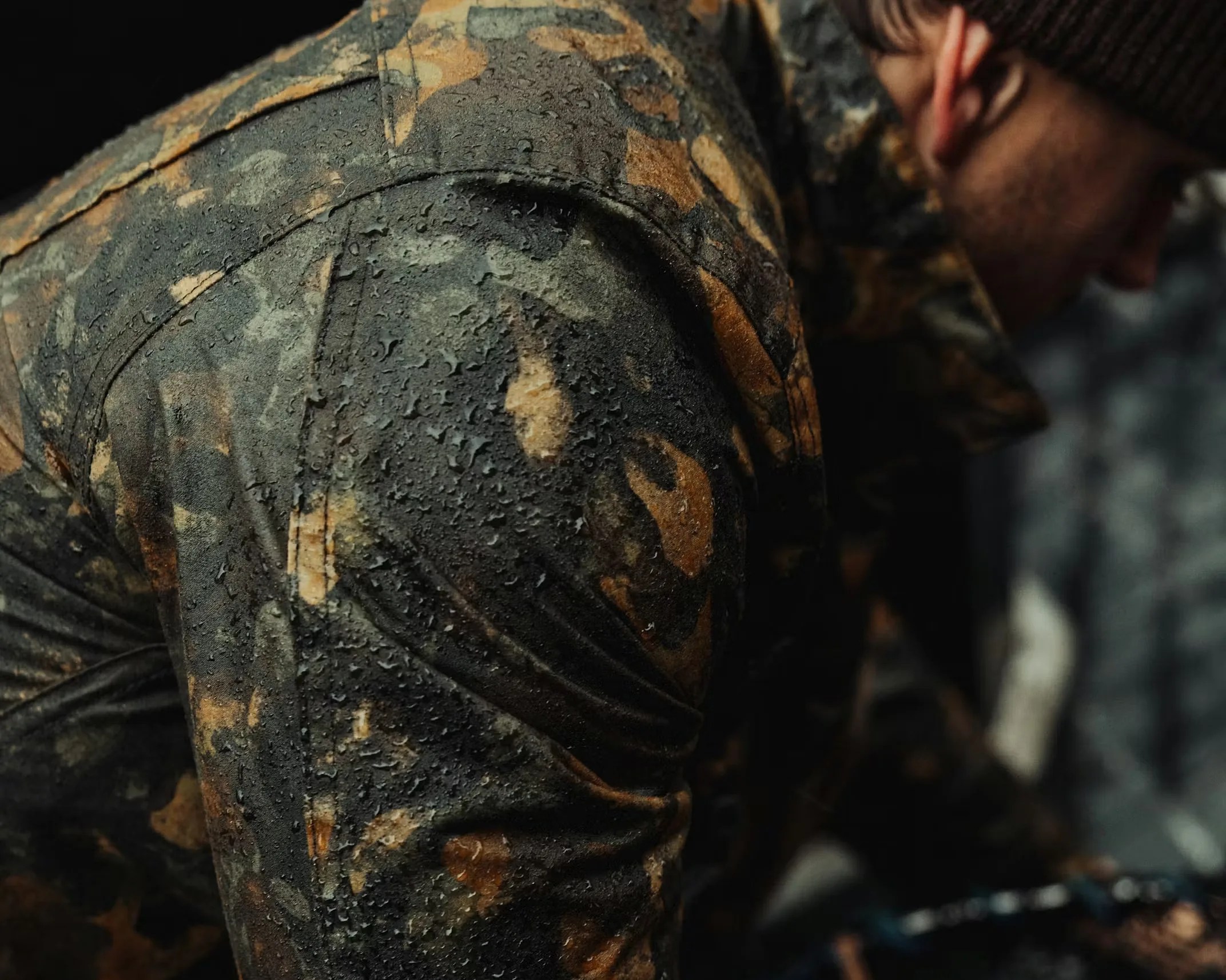 Close-up of a water-resistant camouflage jacket with water droplets on the fabric, worn by a person.