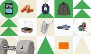 Black bag of Irving Farm New York coffee with blue label on green circle background. Orange U-shaped neck pillow on beige background. Blue geometric pendant on beige and green triangle background. Olive green button-up shirt with chest pockets on green background. Wooden turntable with vinyl record and clear lid on white background. Silver portable cassette player with USB cable on beige background. Two blue vintage toy cars on white background. Collapsible orange and blue camping cookware set with fork on white circle background. Gray speckled Nike dumbbell with metal handle on beige circle background. Bright orange notebook with elastic band on beige background.