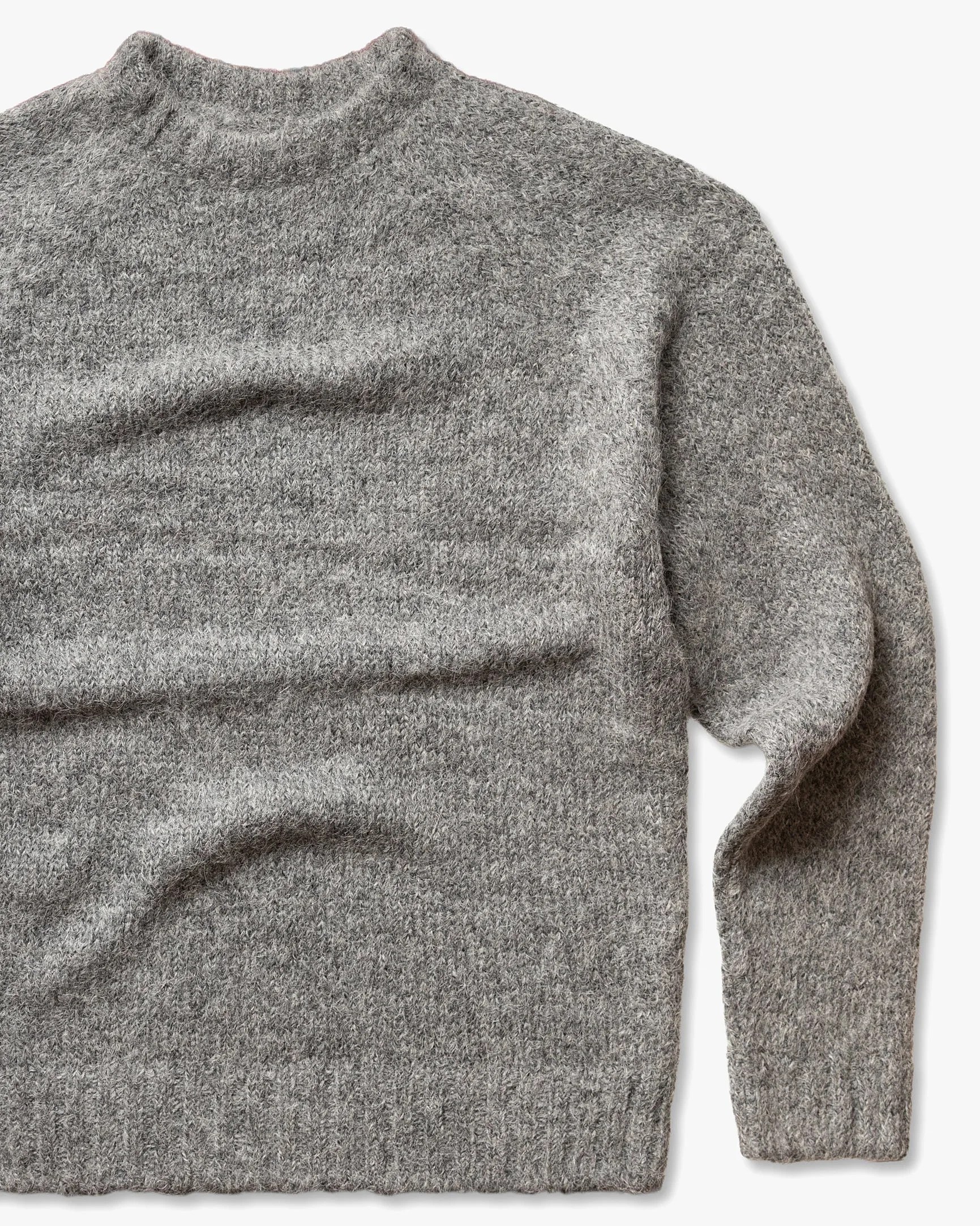 Gray knitted wool sweater with ribbed cuffs and hem laid flat on a white background.