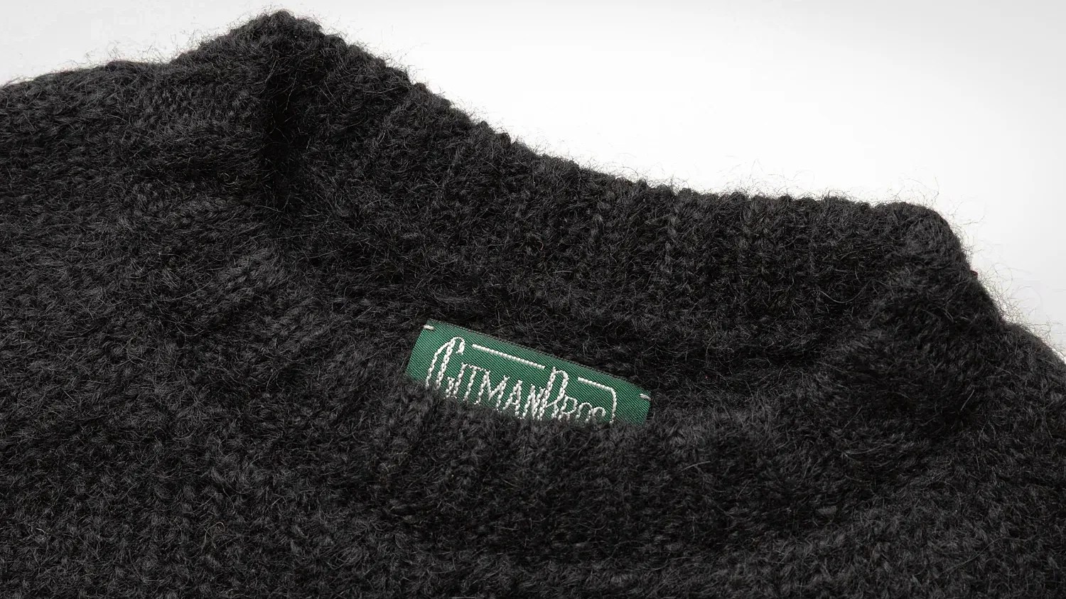 Close-up of a black fuzzy knit sweater collar with a green label partially visible inside.
