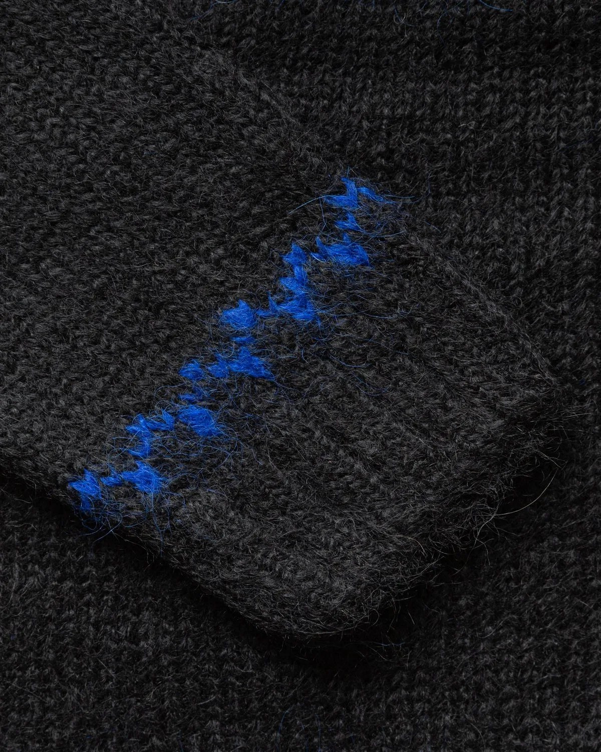 Close-up of black knitted fabric with a ribbed cuff featuring a blue zigzag stitch detail.