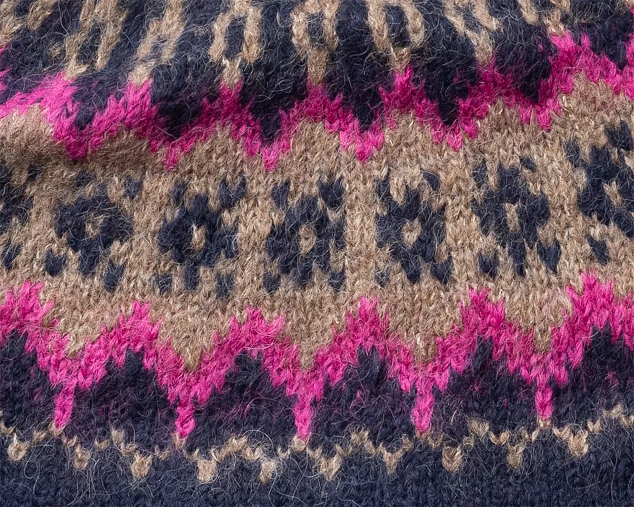 Close-up of knitted fabric with a pattern of navy blue, beige, and bright pink zigzags and shapes.