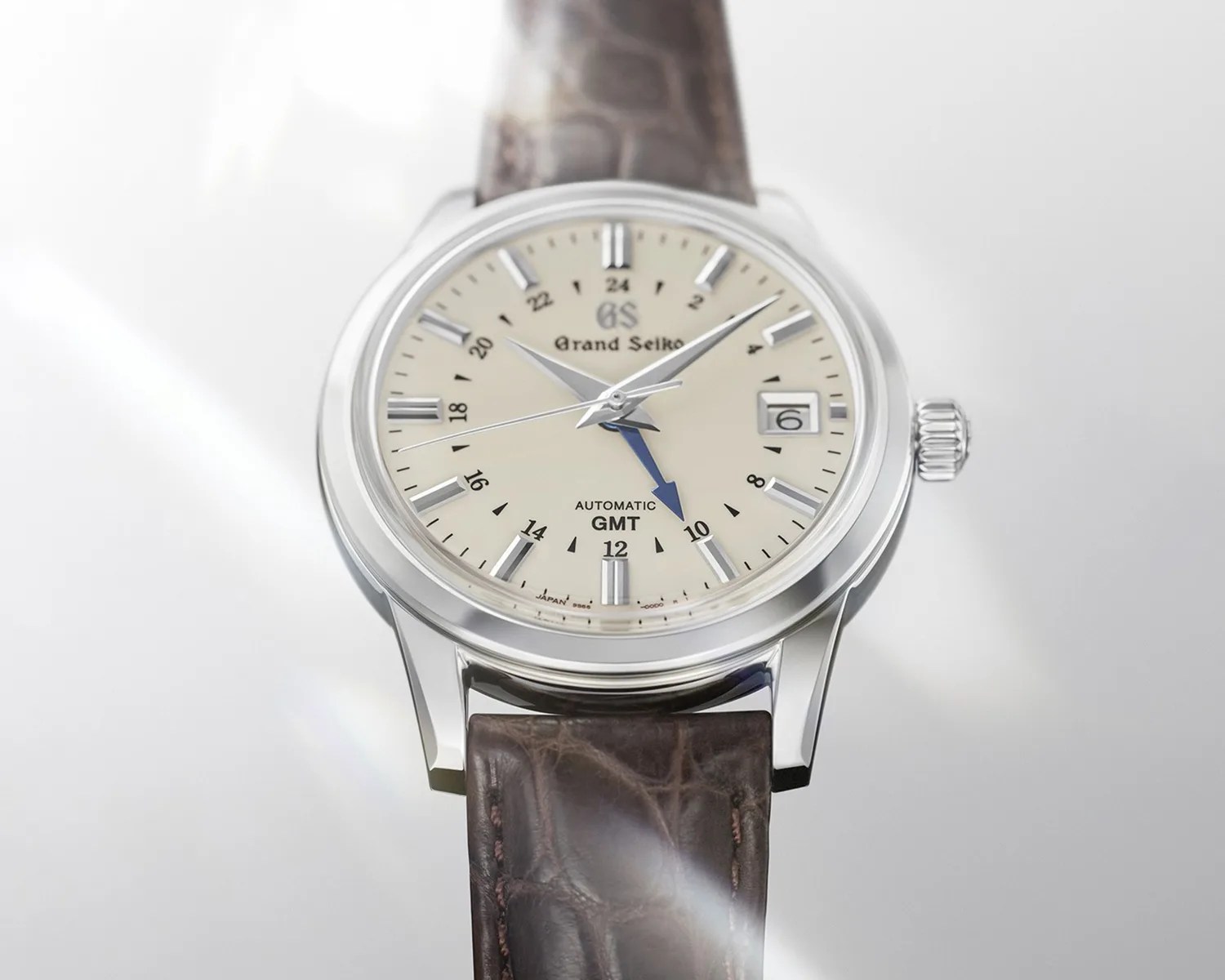 Grand Seiko wristwatch with cream dial, silver hour markers, blue GMT hand, date window, and brown leather strap.