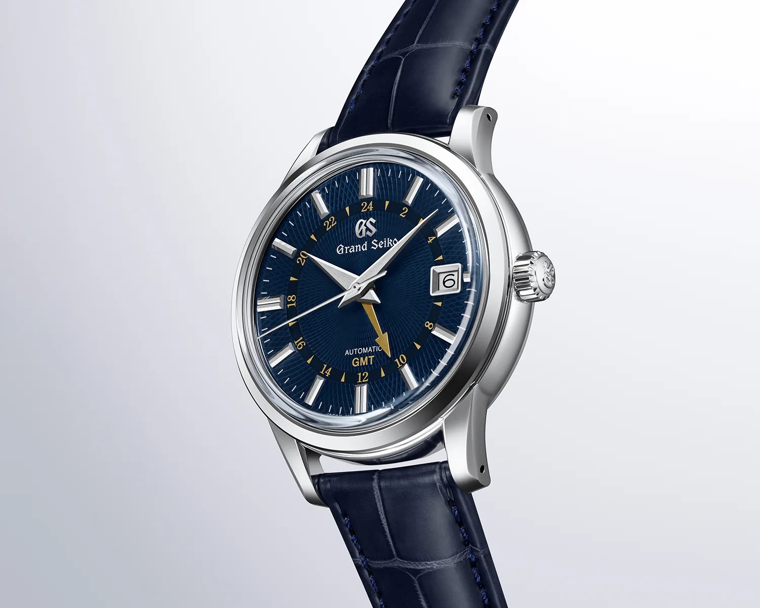 Silver Grand Seiko wristwatch with blue textured dial, yellow GMT hand, date window, and blue leather strap.