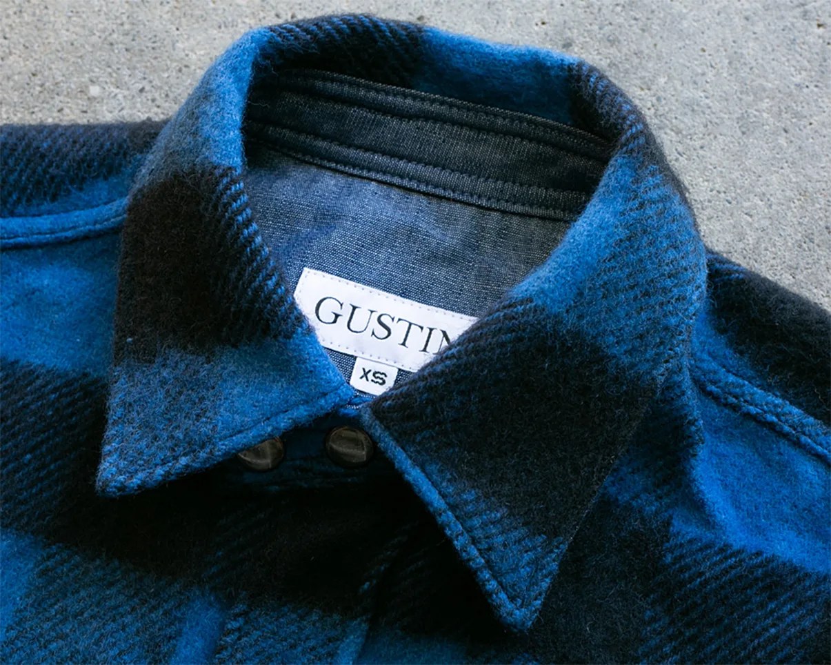 Close-up of a blue and black plaid wool shirt collar with a "GUSTIN" label and XS size tag.