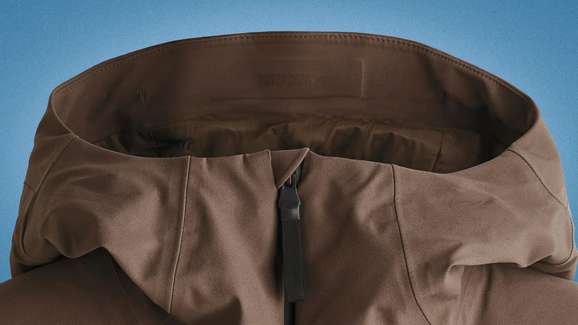 Brown jacket hood with a black zipper pull tab against a blue background.