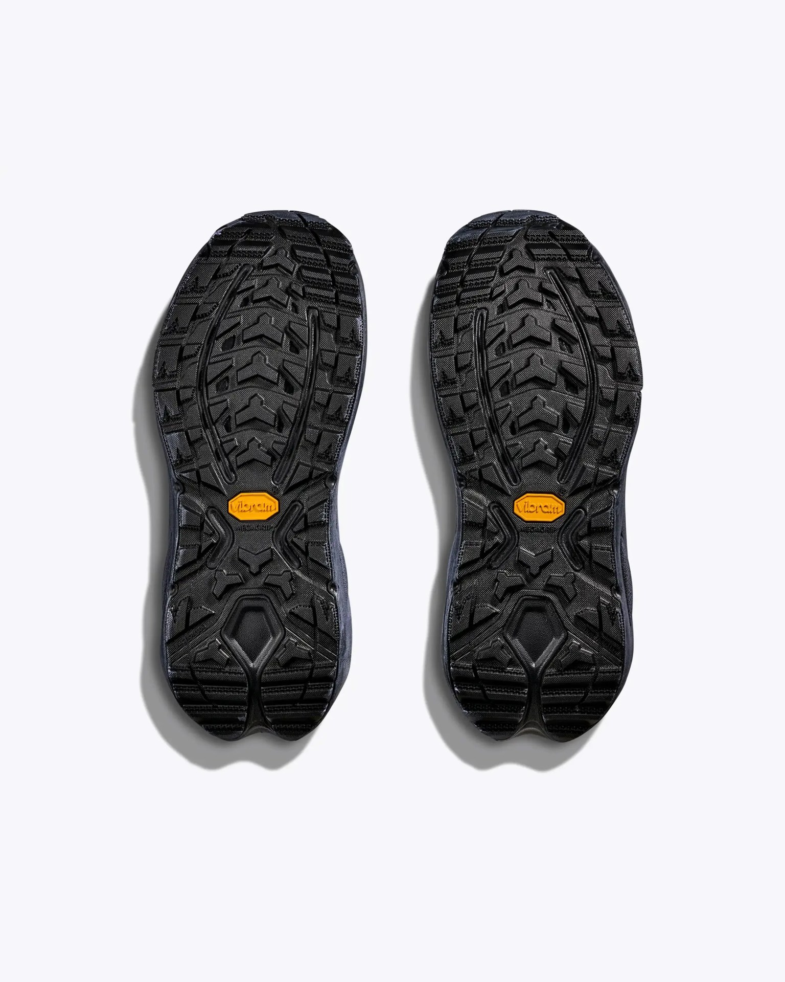 Pair of black Vibram rubber shoe soles with deep treads and an orange Vibram logo in the center.