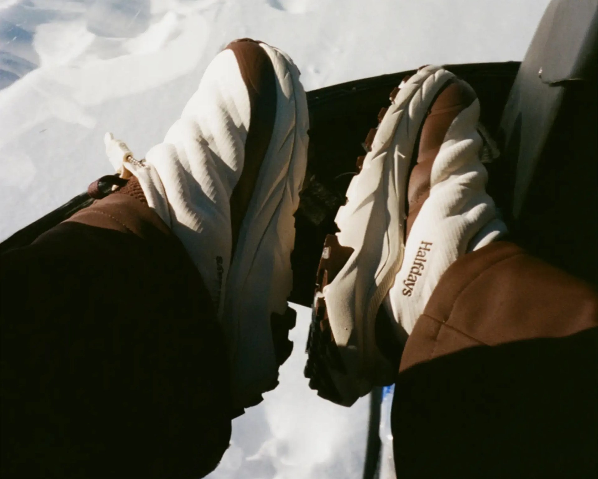 White and brown Halfdays sneakers worn with brown pants against a snowy background.