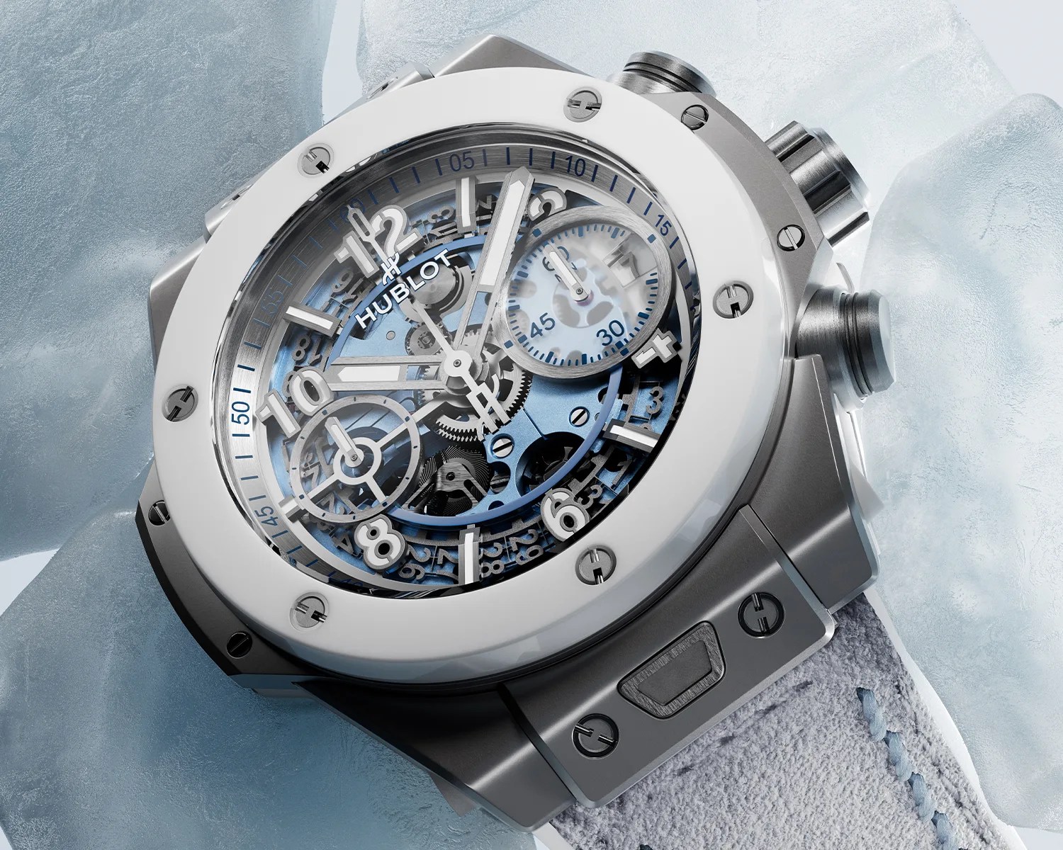 Silver Hublot wristwatch with a blue skeleton dial and white ceramic bezel on a light gray strap.