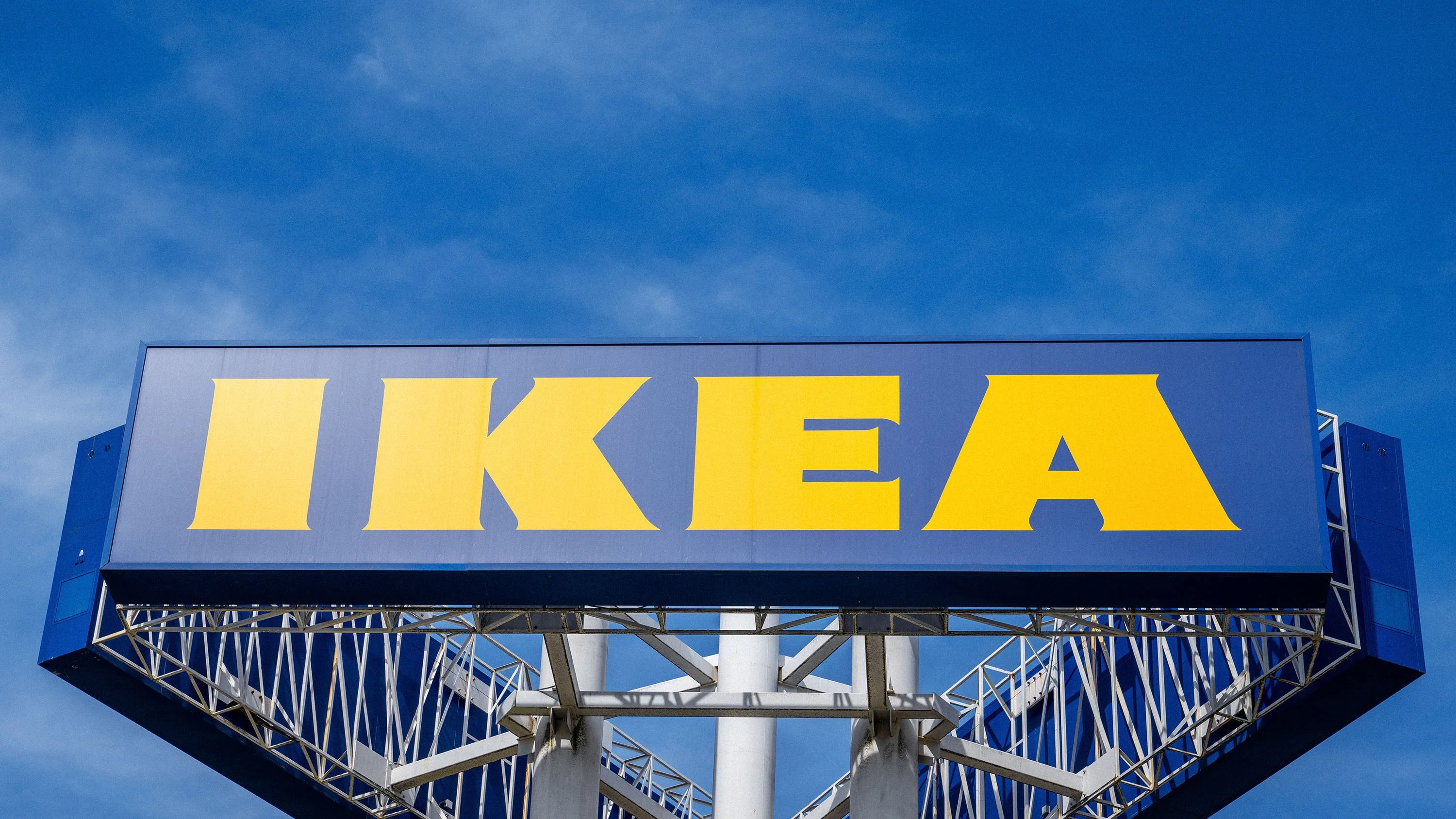 Large blue IKEA sign with bold yellow letters mounted on a metal structure against a blue sky.