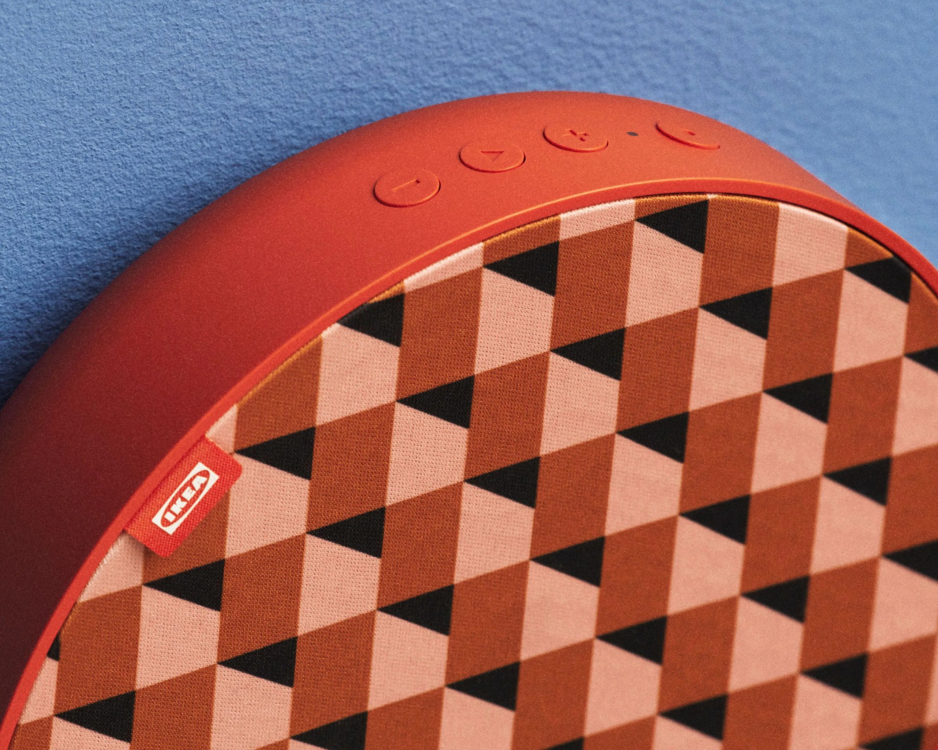 Round red IKEA Bluetooth speaker with geometric patterned fabric front against a blue wall.