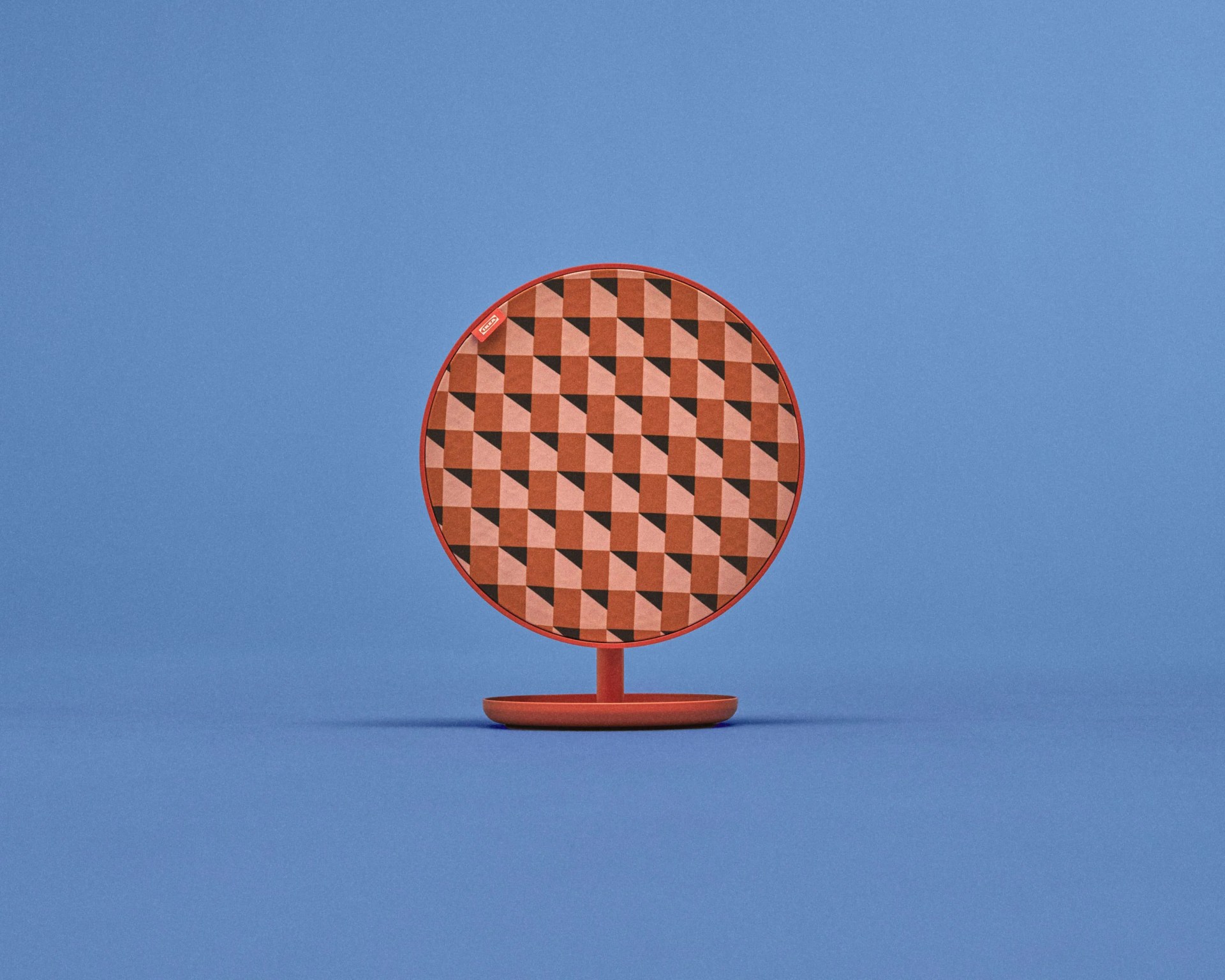 Round red wireless speaker with geometric patterned fabric front on a blue background.