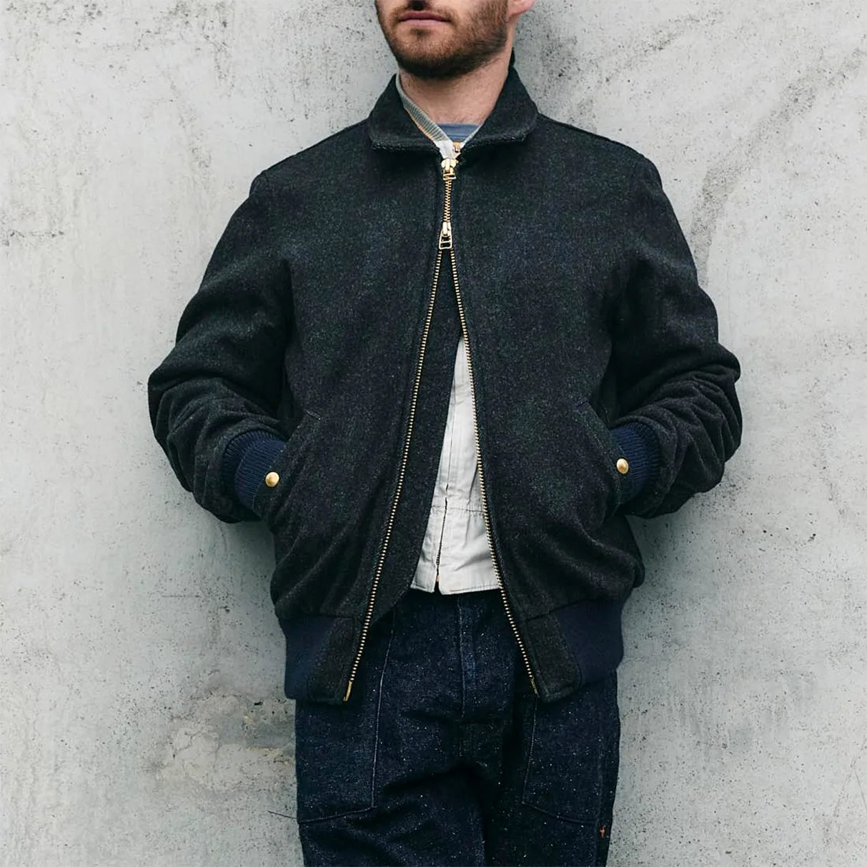 Dark gray wool bomber jacket with gold zipper and snap buttons worn over a white shirt and dark pants.