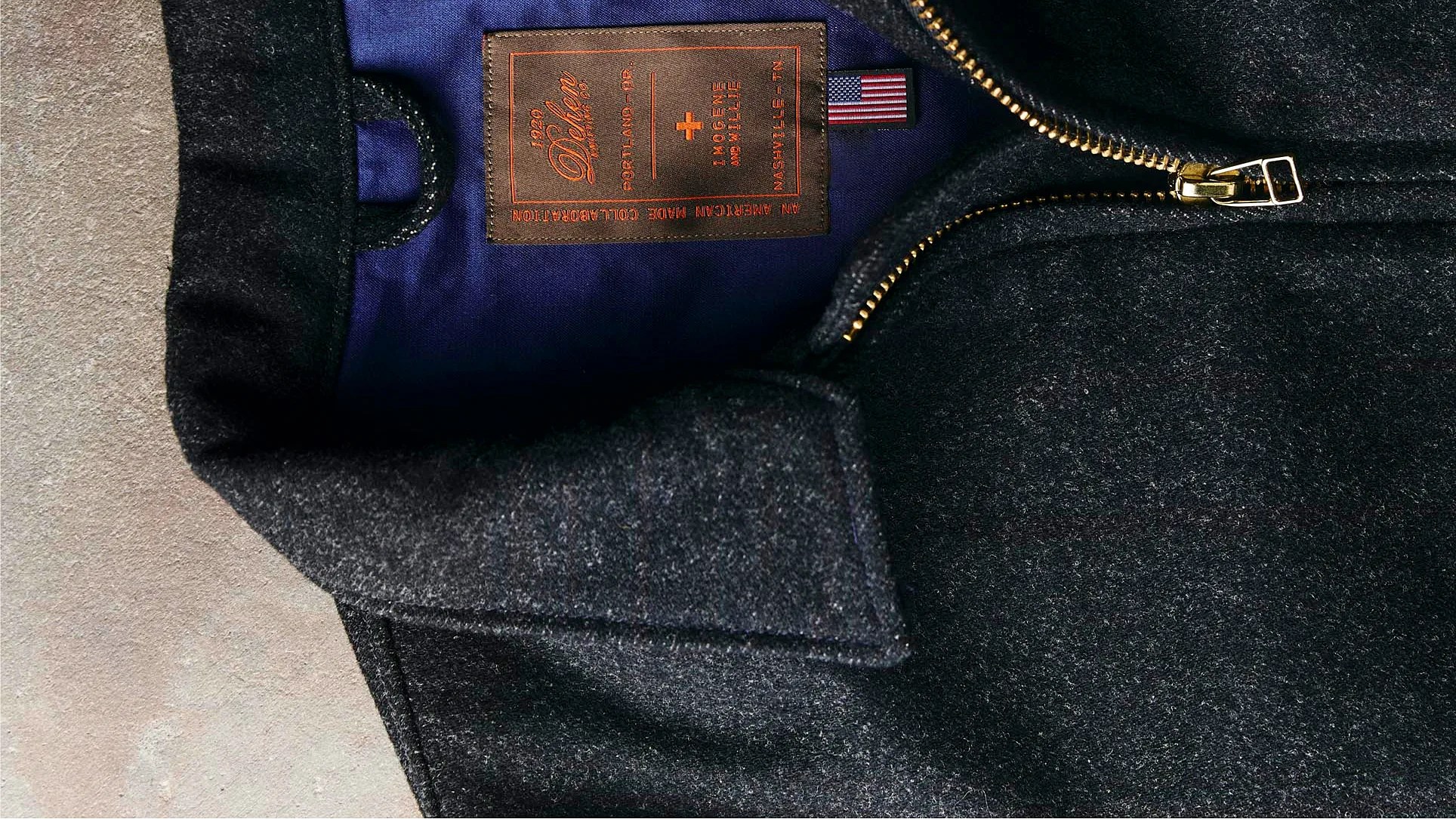 Close-up of a dark wool jacket with a gold zipper and a brown label reading "1920 Deluxe" on a blue inner lining.