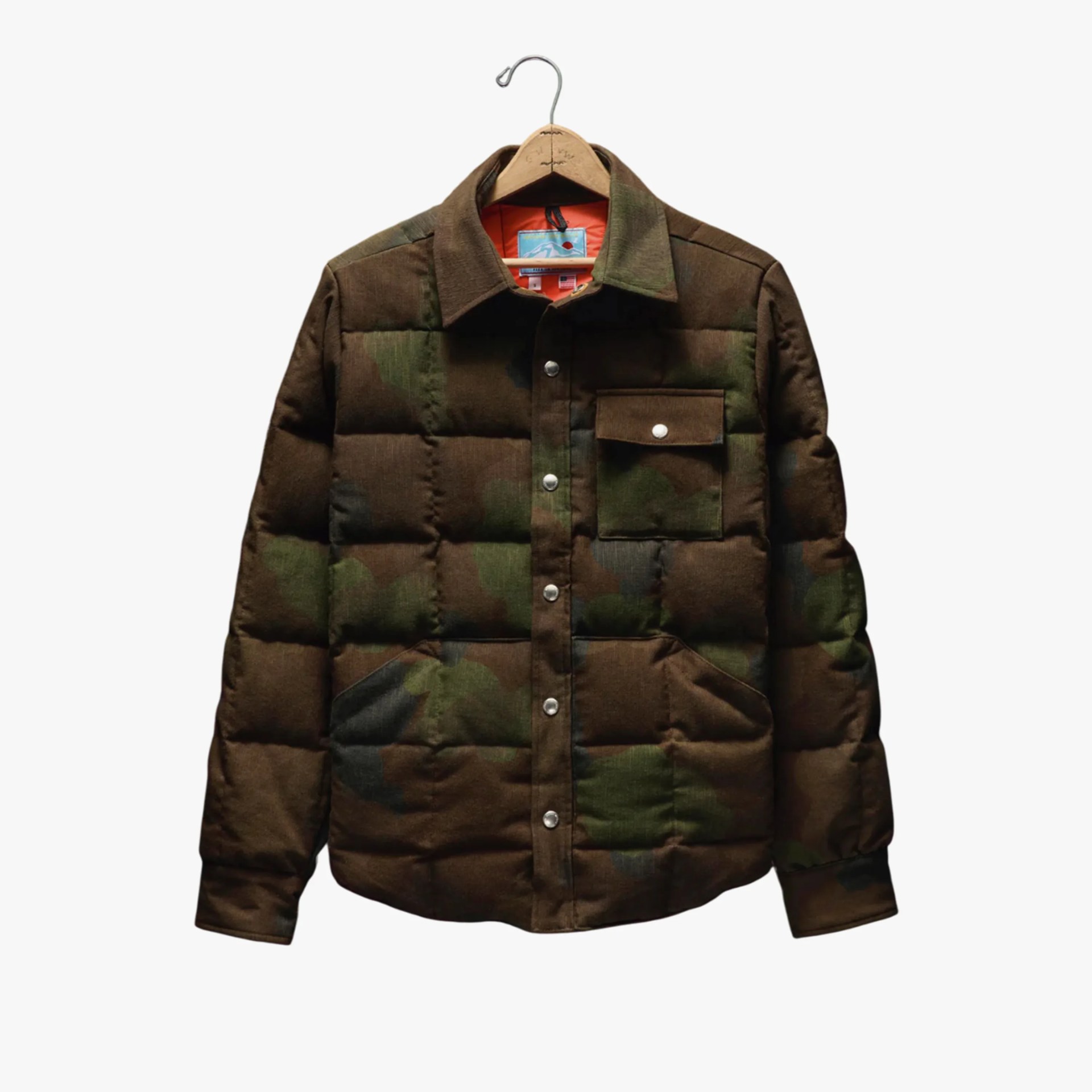 Brown and green camouflage quilted jacket with snap buttons and a chest pocket on a wooden hanger.