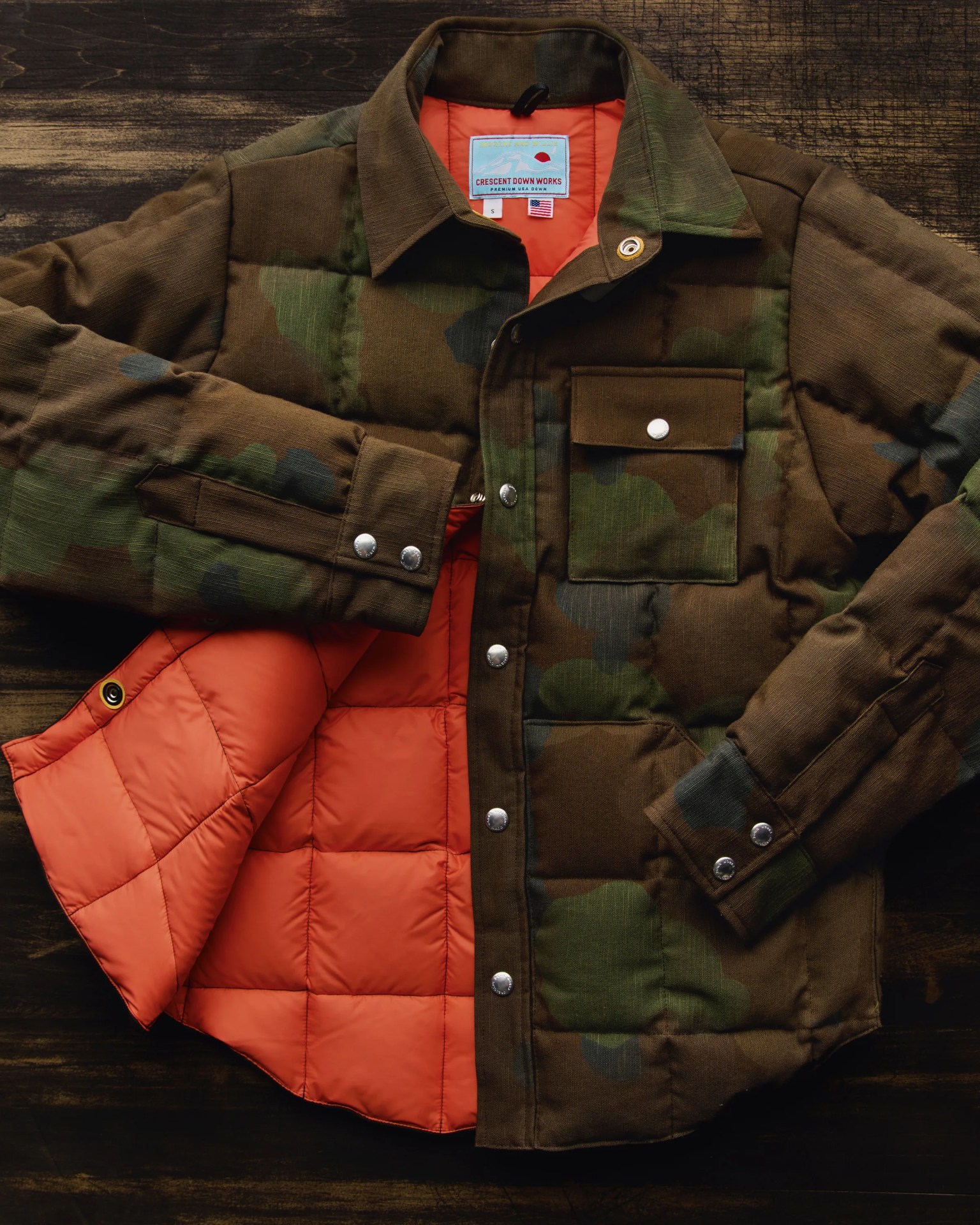Brown and green camouflage quilted jacket with silver snap buttons and bright orange quilted lining.