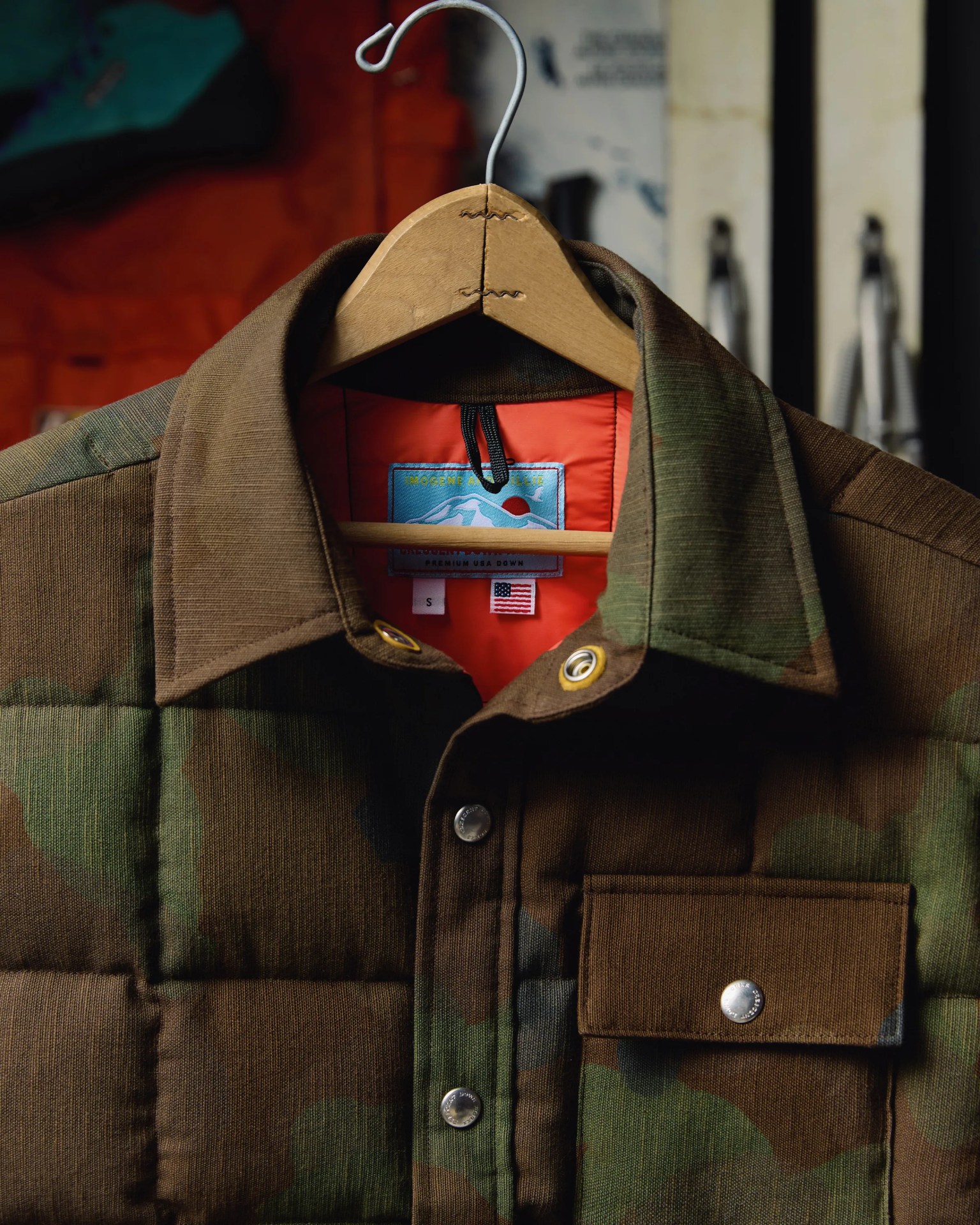Camouflage-patterned quilted jacket with brown collar and snap buttons on a wooden hanger.