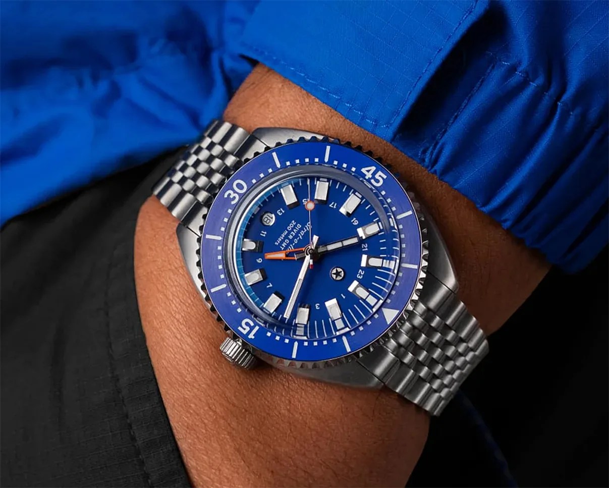 Stainless steel dive watch with blue bezel and dial, worn on a wrist with a blue sleeve.