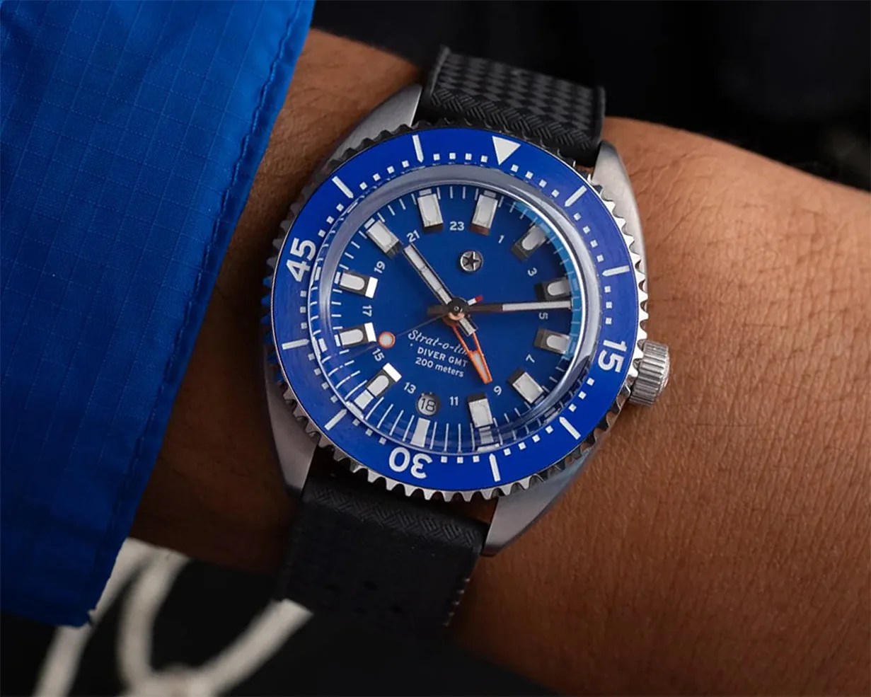 Blue diver GMT watch with silver bezel and black textured strap worn on a wrist.
