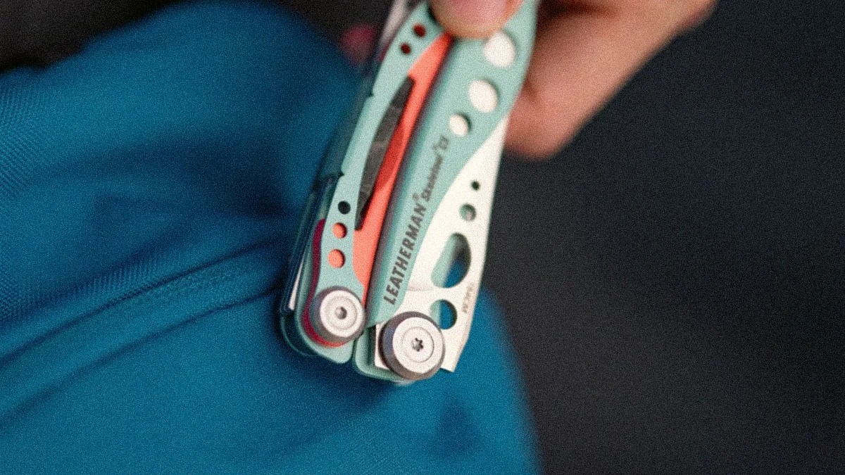 Folded teal Leatherman multi-tool held in a hand against a dark background.