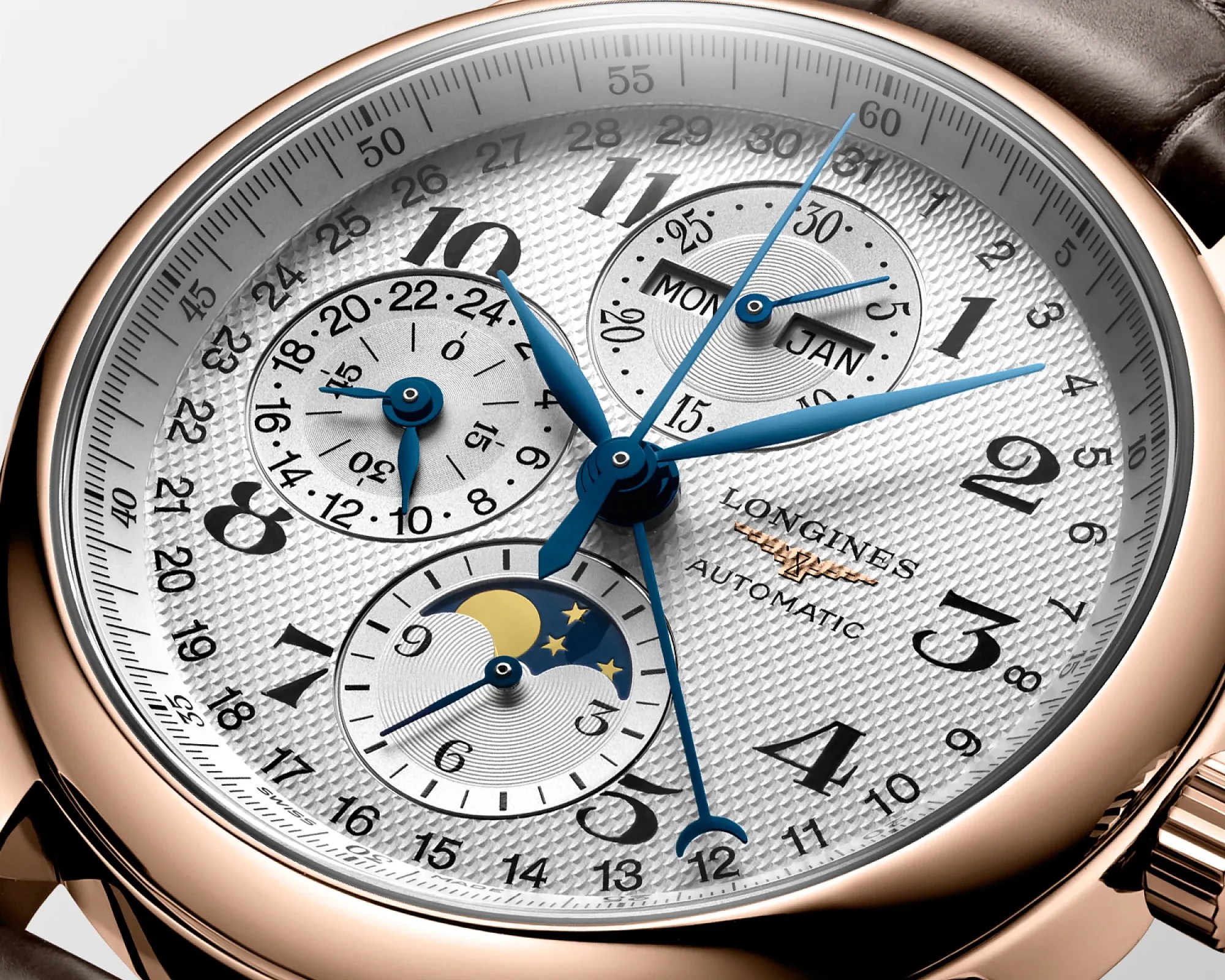 Close-up of a Longines automatic watch with a white textured dial, blue hands, moon phase, and calendar subdials in a rose gold case.